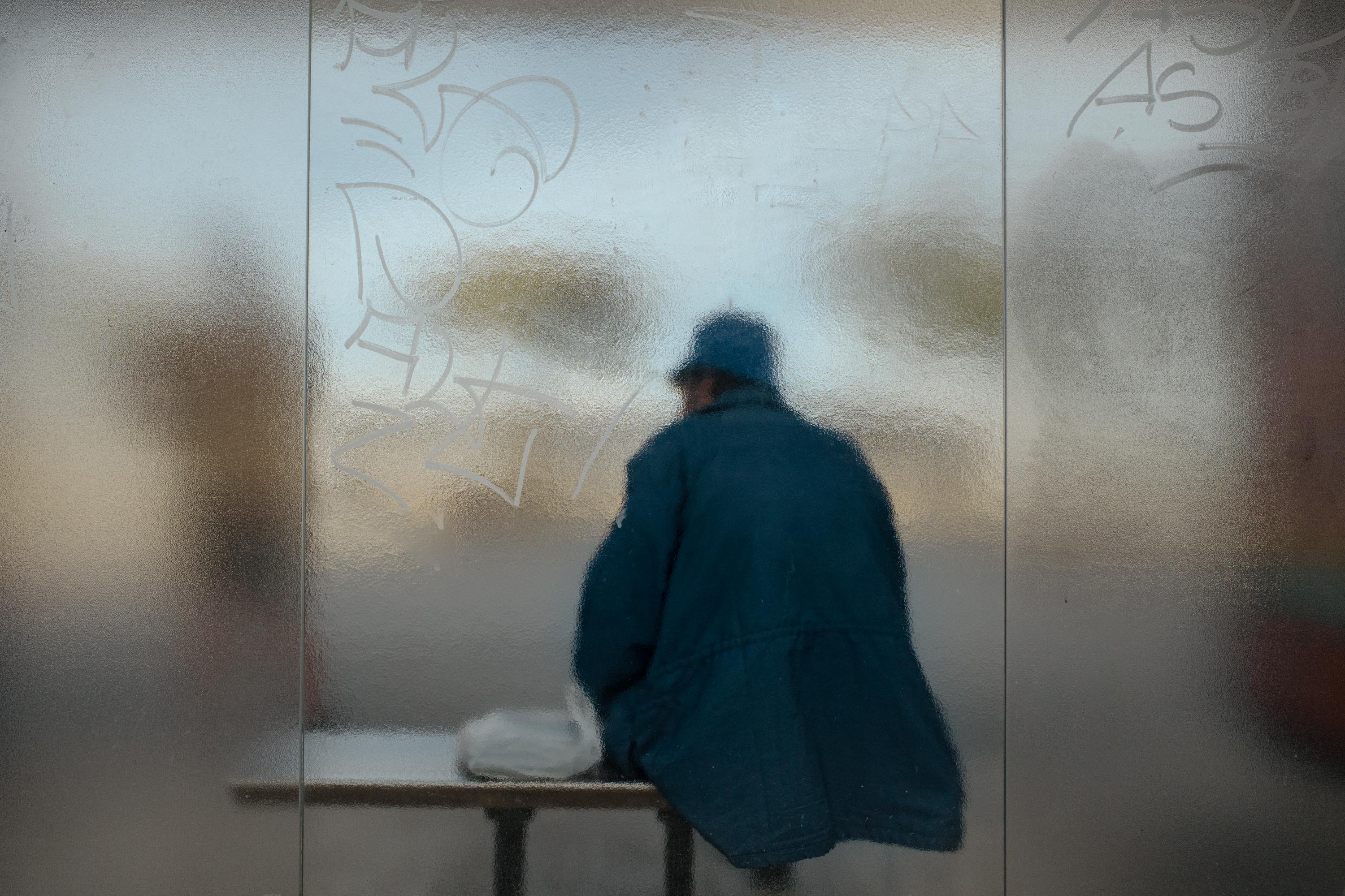 Ein Mann sitzt hinter der Milchglasscheibe einer Bushaltestelle