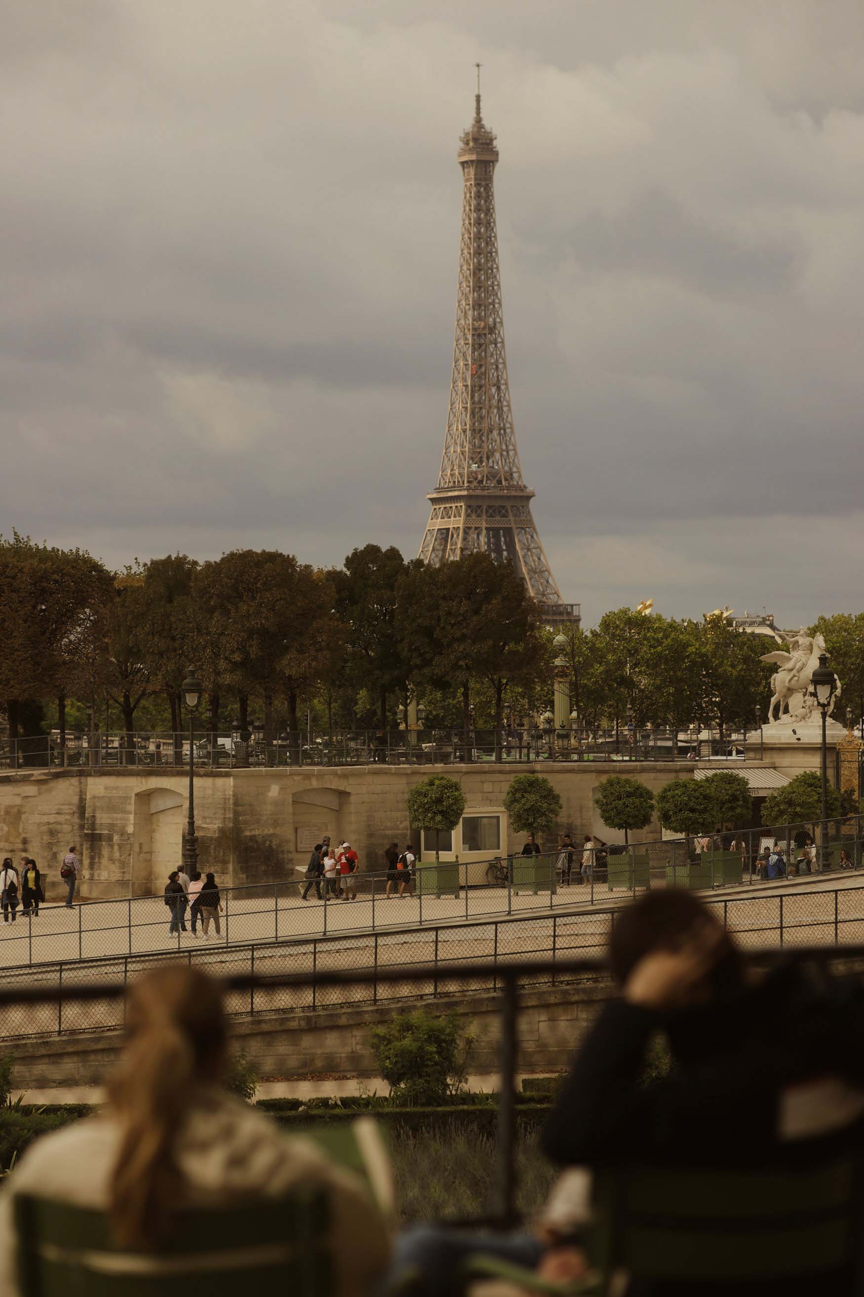 In the foreground, an out-of-focus couple sit on chairs while looking out at the Eiffel Tower in the background