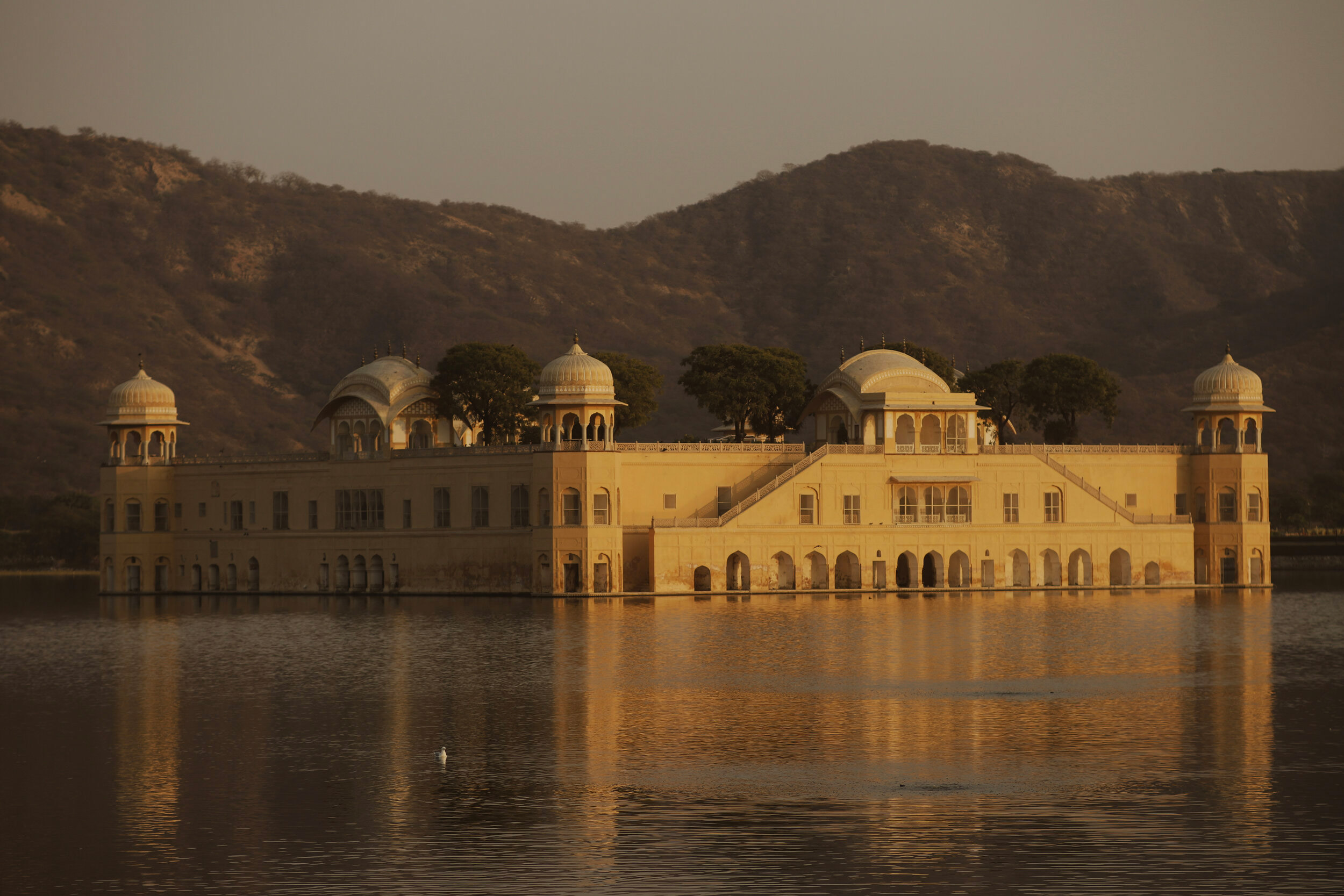 A large building reflecting onto a river in the foreground, with a mountain in the background.