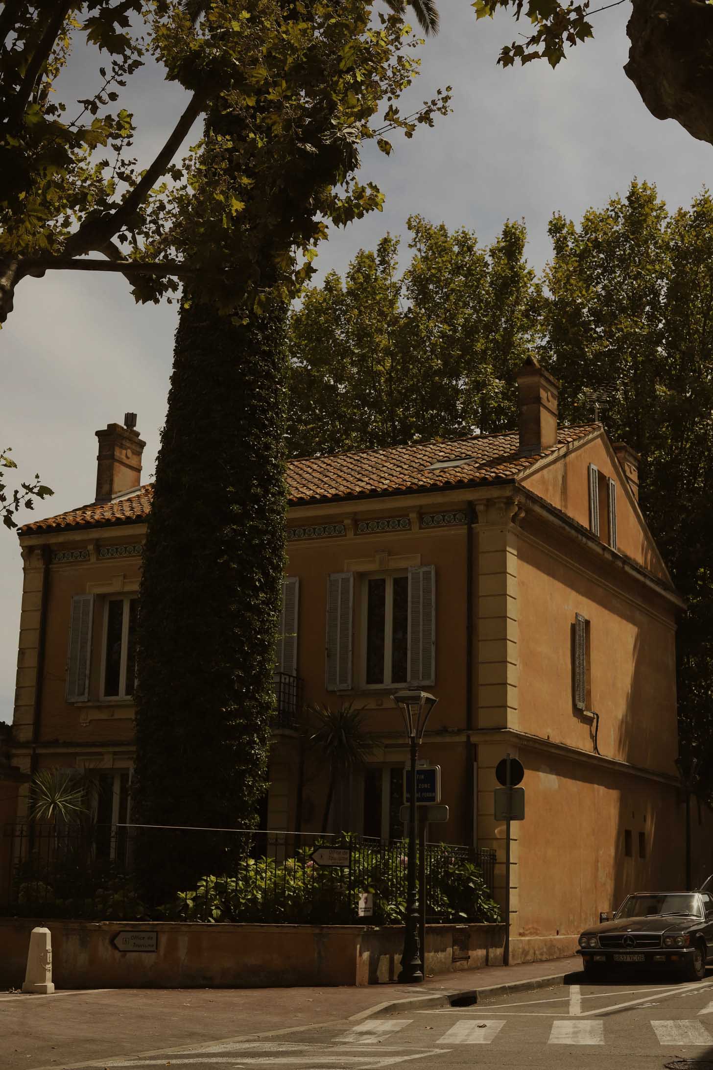 A villa in southern France with a large tree growing in front of it and a car on the road next to it