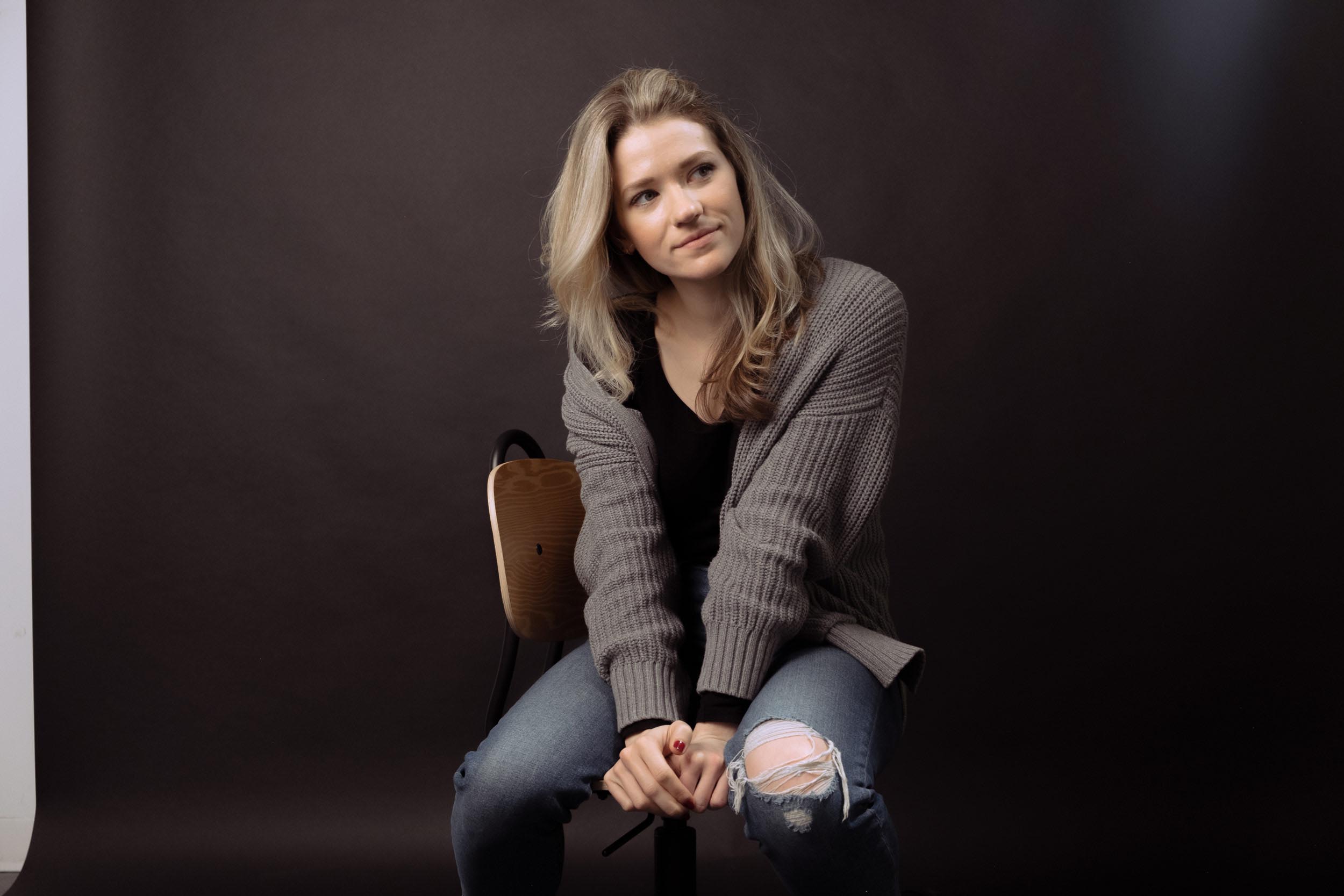 Model poses on chair in front of black backdrop