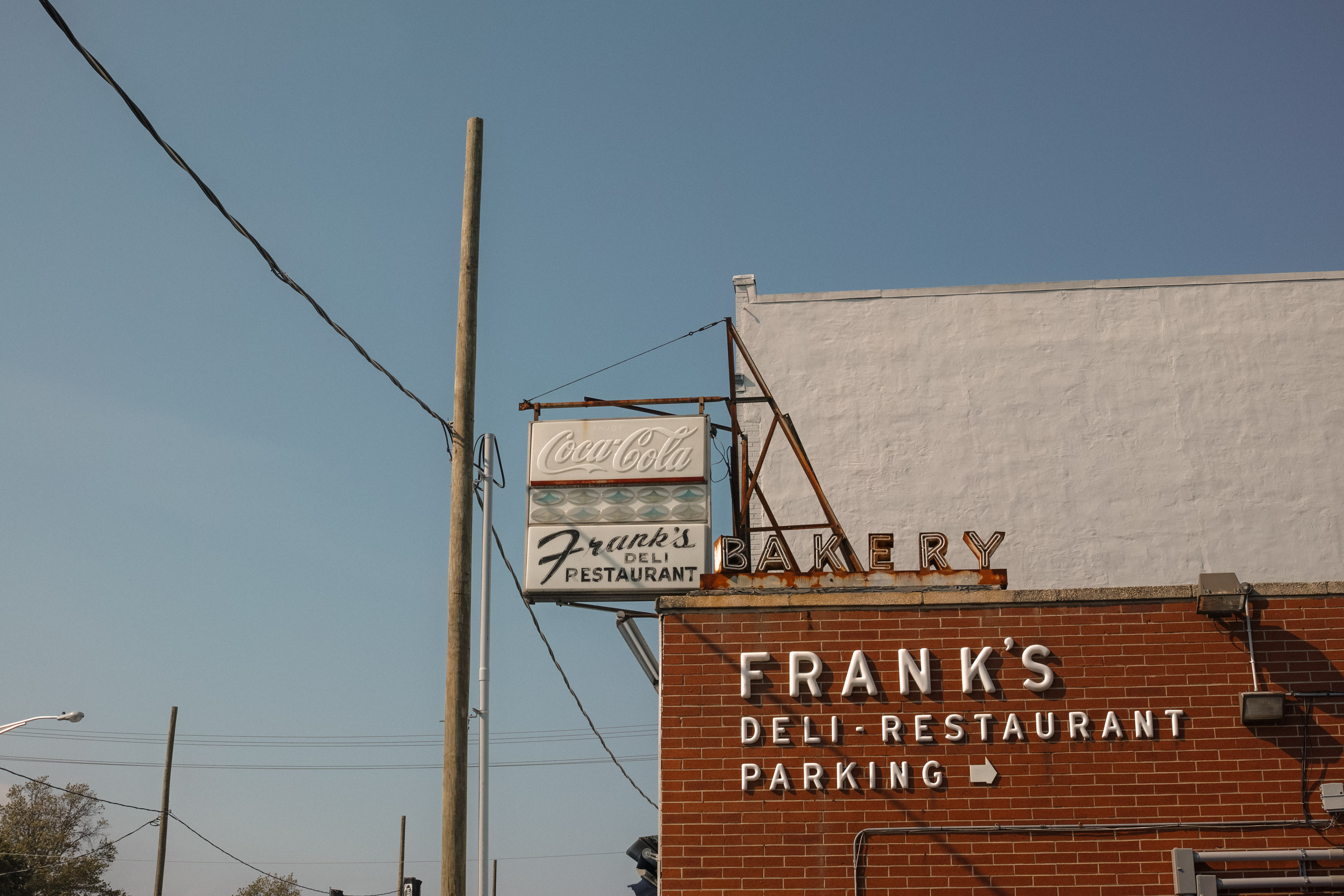 A building with signage displaying ”Frank’s Deli and Restaurant” against a blue sky with power lines and pole 