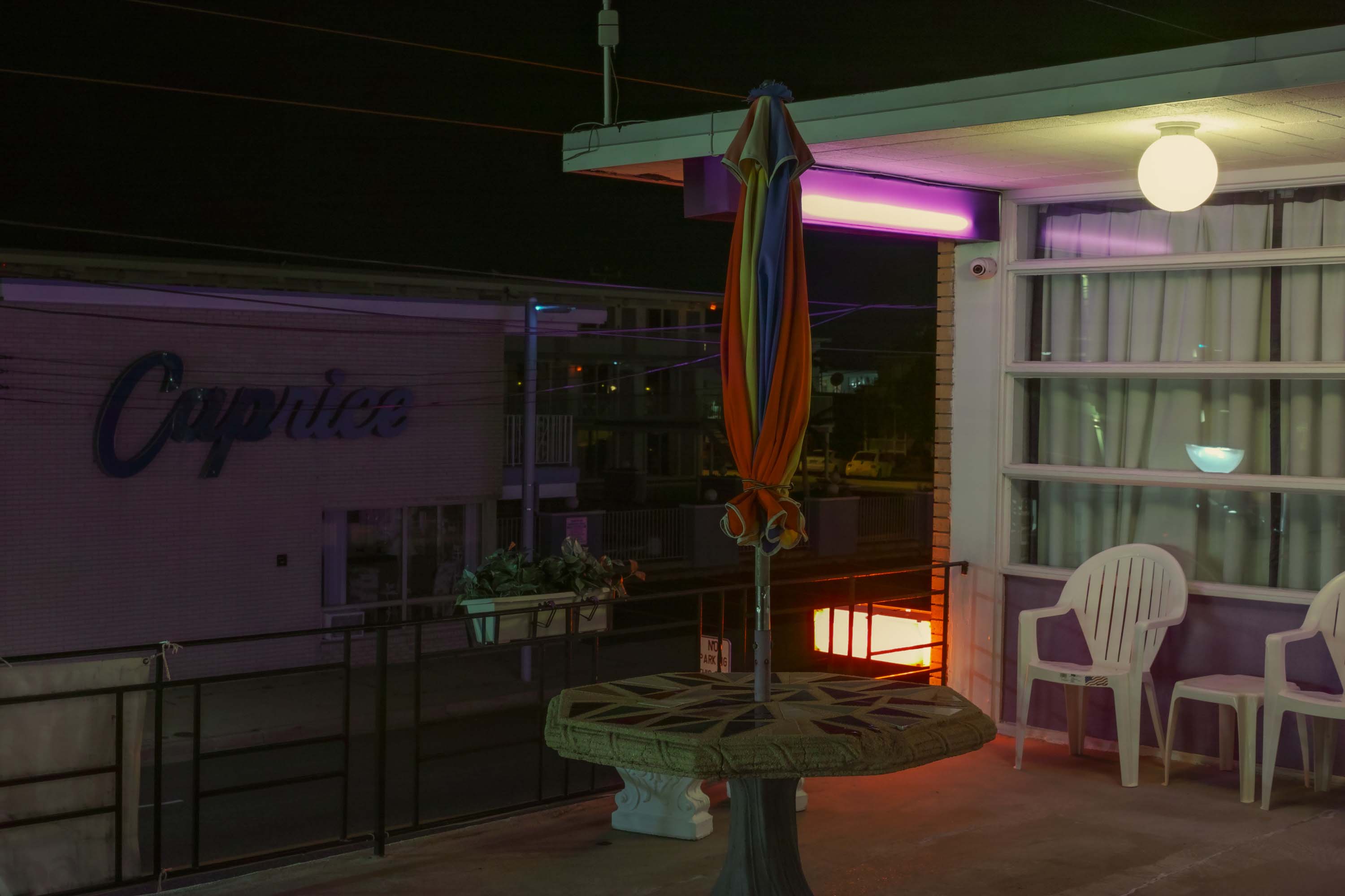 A low-light image of a motel with neon lights and plastic outdoor furniture