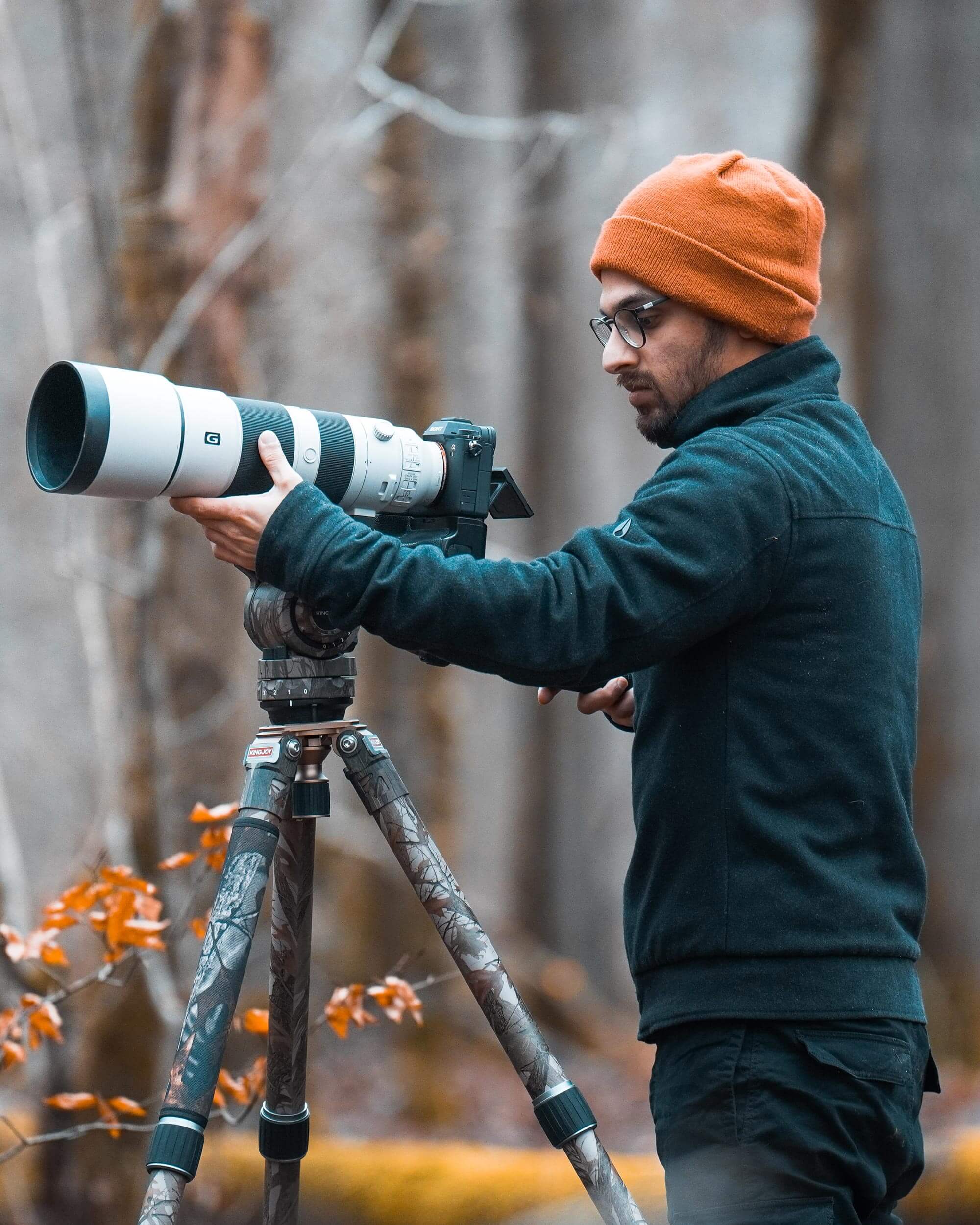 Fotograaf Sasan Amir met een oranje muts en een camera op een statief in het bos.
