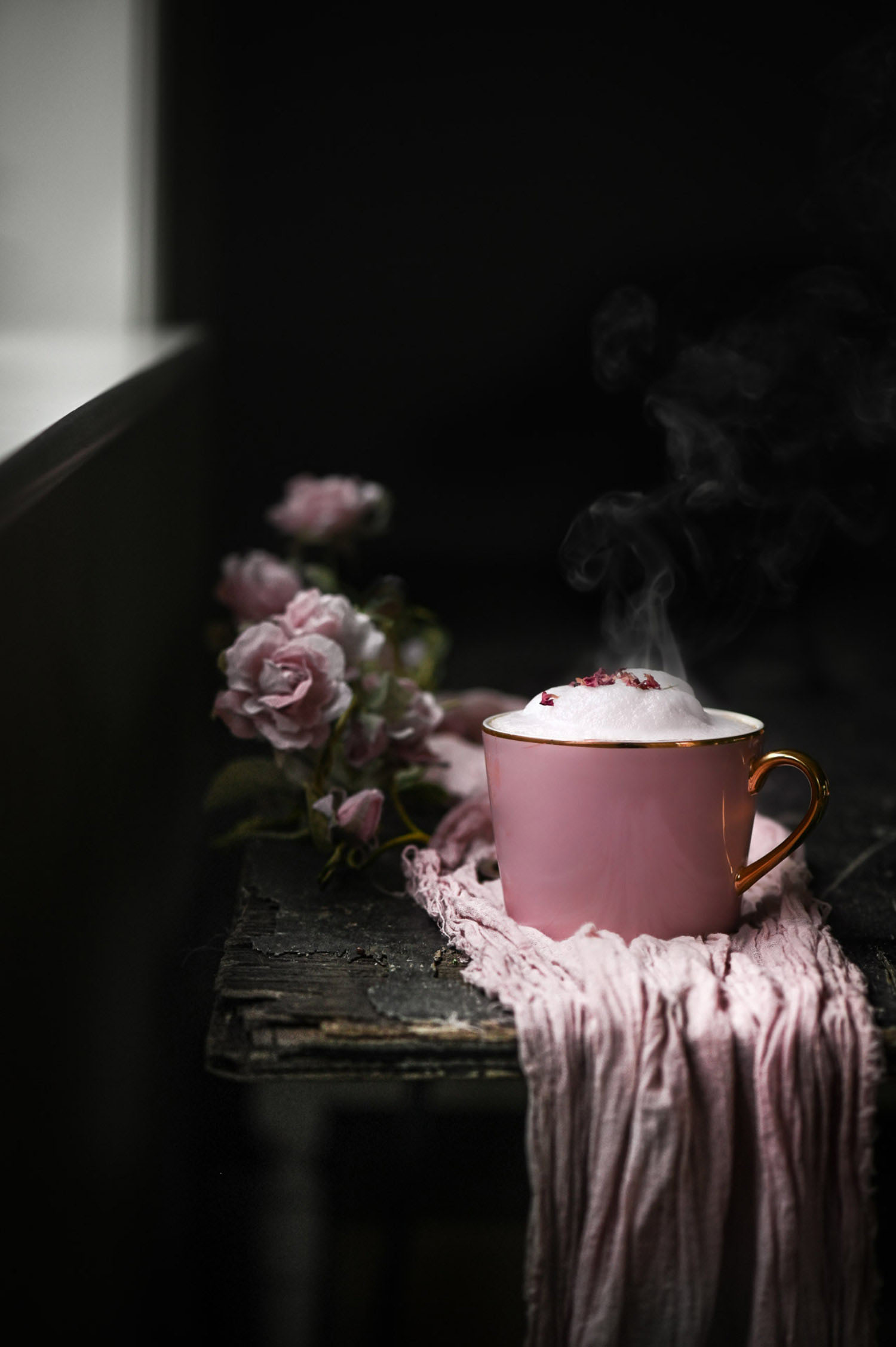A purple cup on top of a purple cloth on a table, with roses next to it. Foam is coming out of the top of the mug.