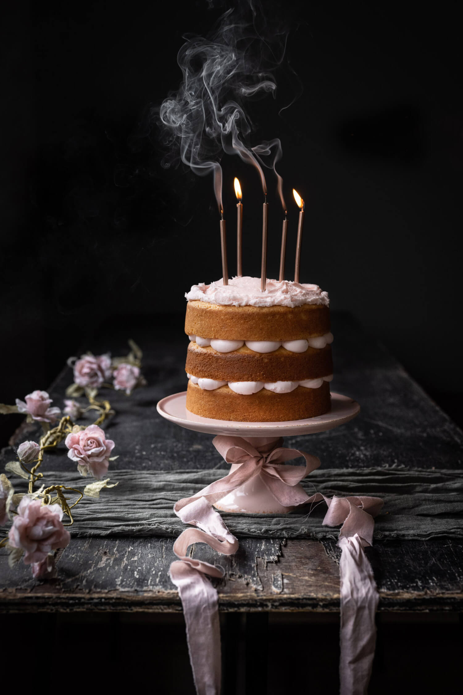 a three-tiered cake sits on a cake stand, with five candles in, three of which have gone out.
