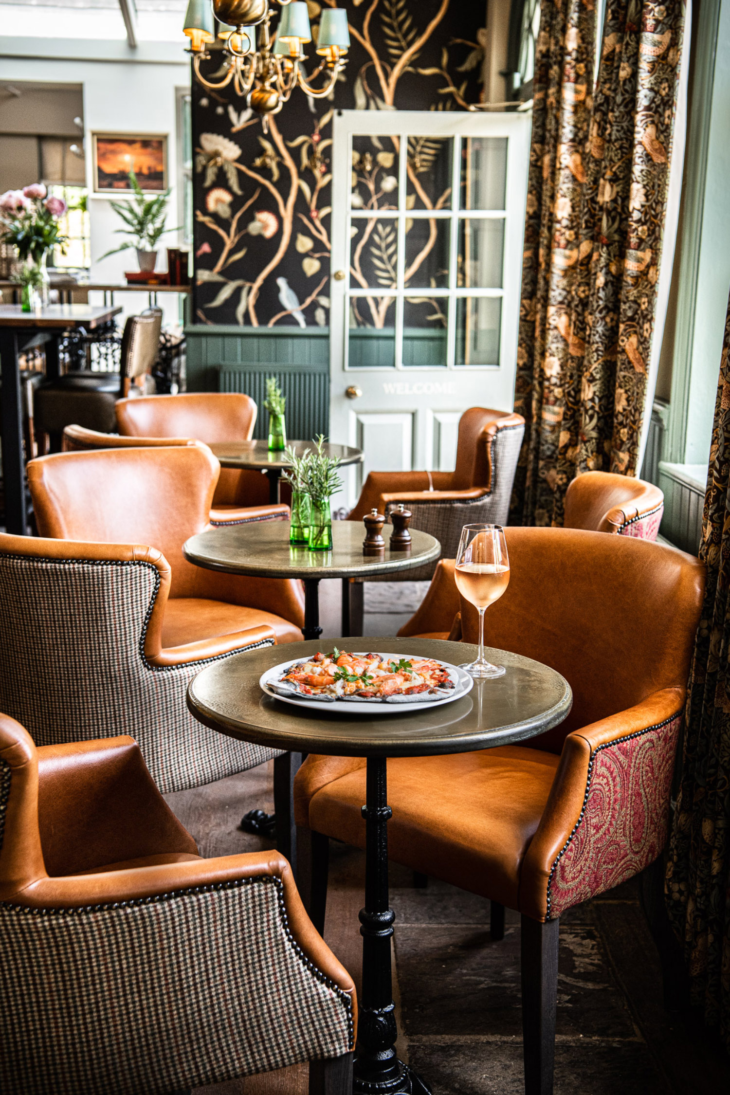 three tables in a restaurant, one with a pizza and a glass of wine