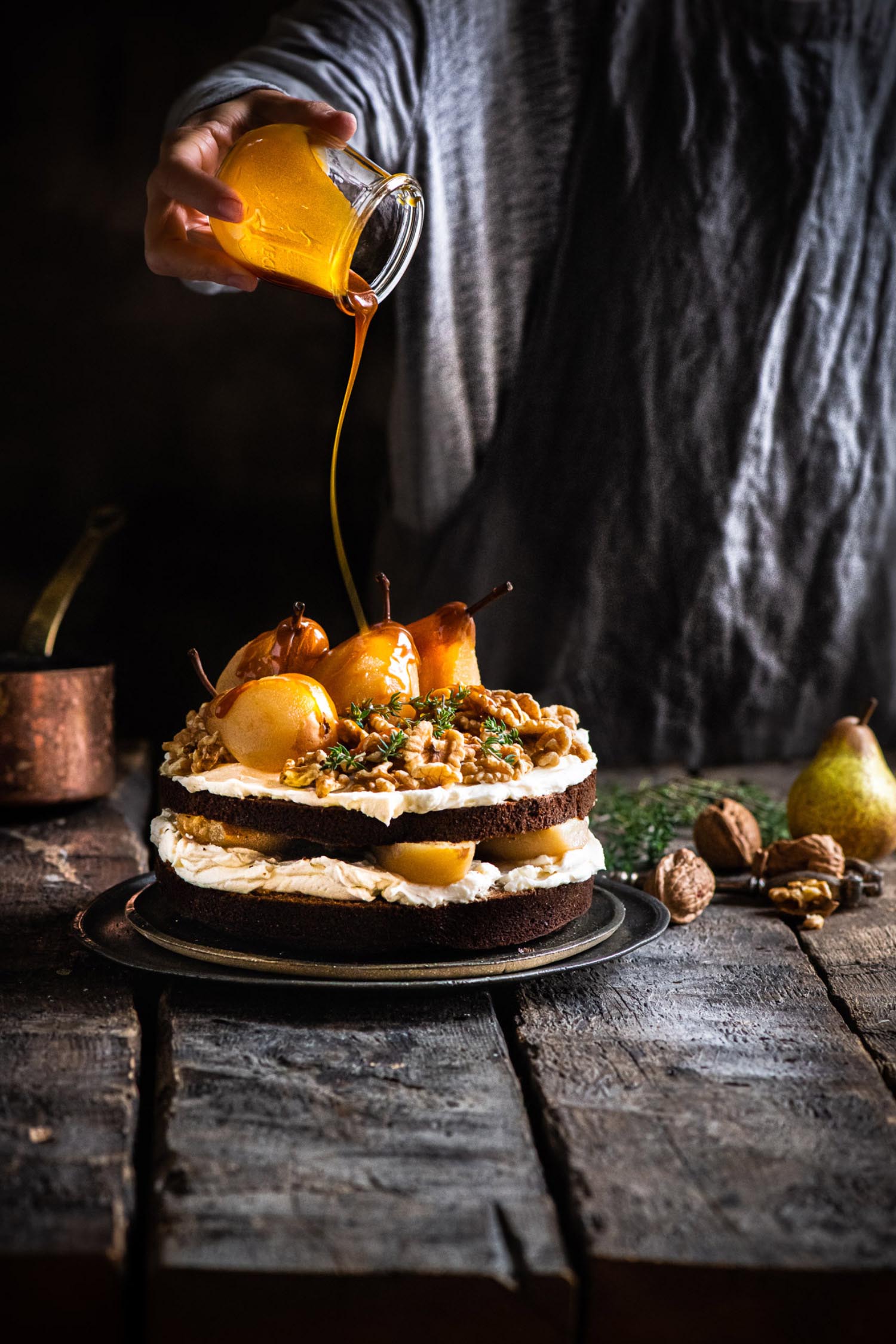 a jar of honey is poured on top of a two-tiered cake which has pairs on top