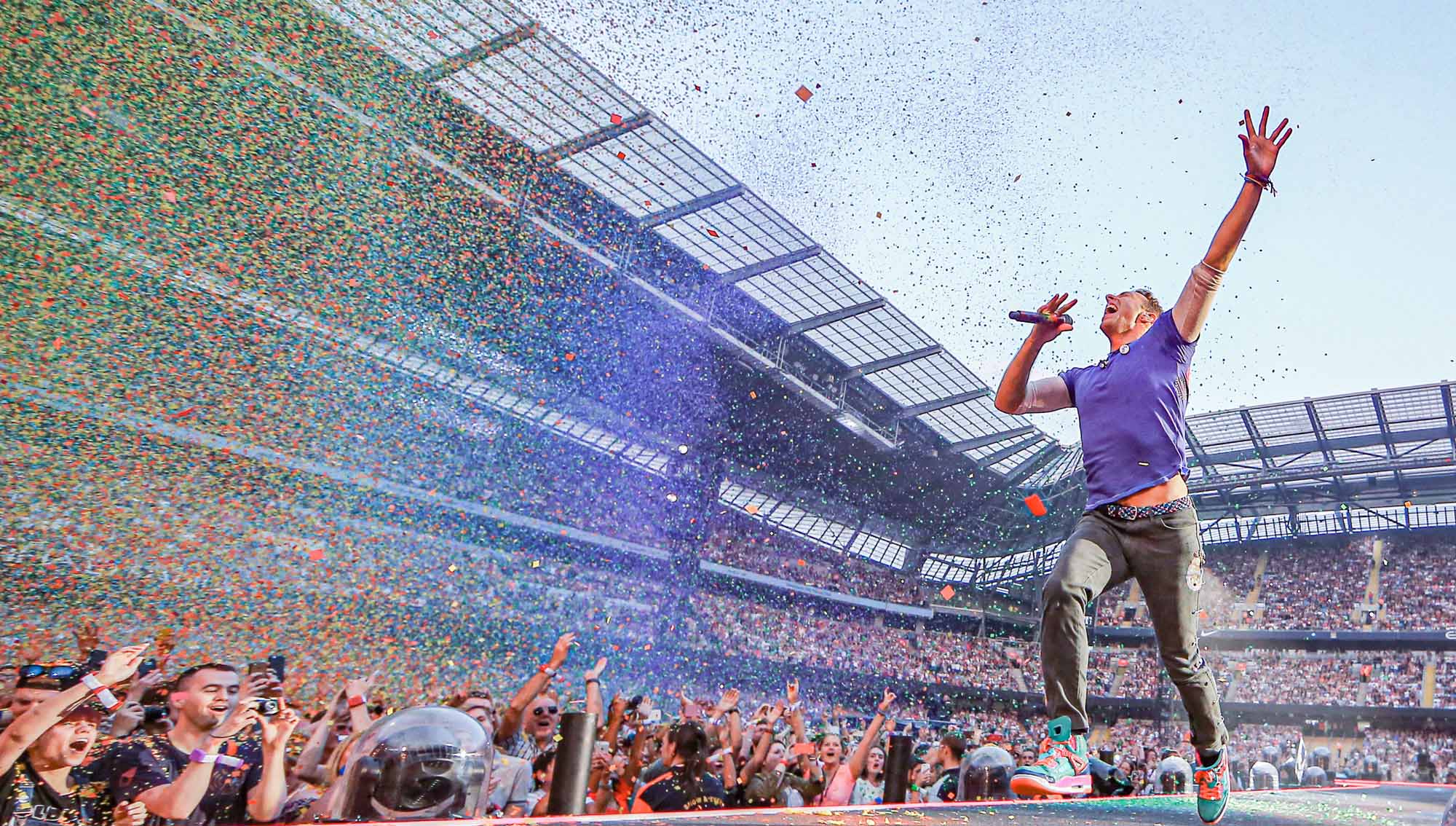 Chris Martin of Coldplay runs down a walkway while performing live at a stadium.