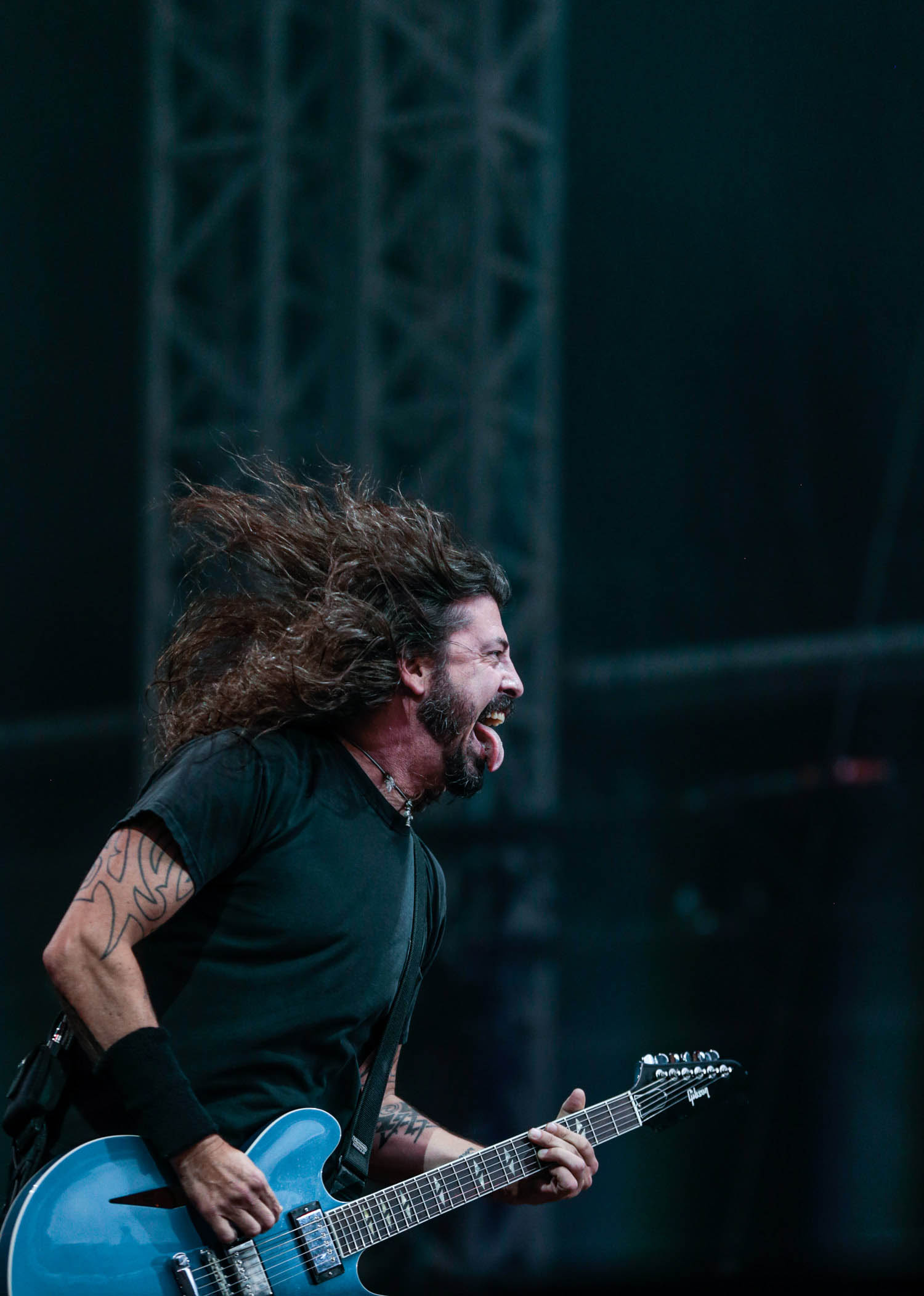 Dave Grohl playing a blue guitar on stage while sticking his tongue out.