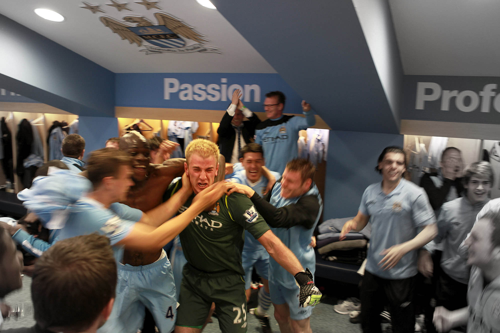 Manchester City players celebrate in their dressing room, many players appear out of focus, except Joe Hart.