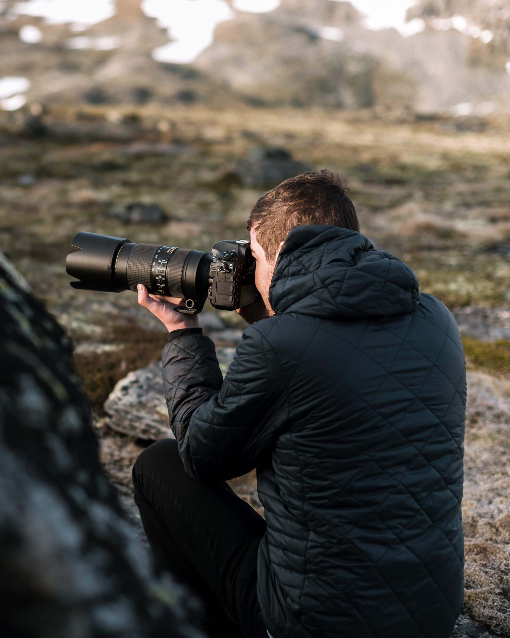 A photographer from the back, sitting down and holding his camera to take a picture