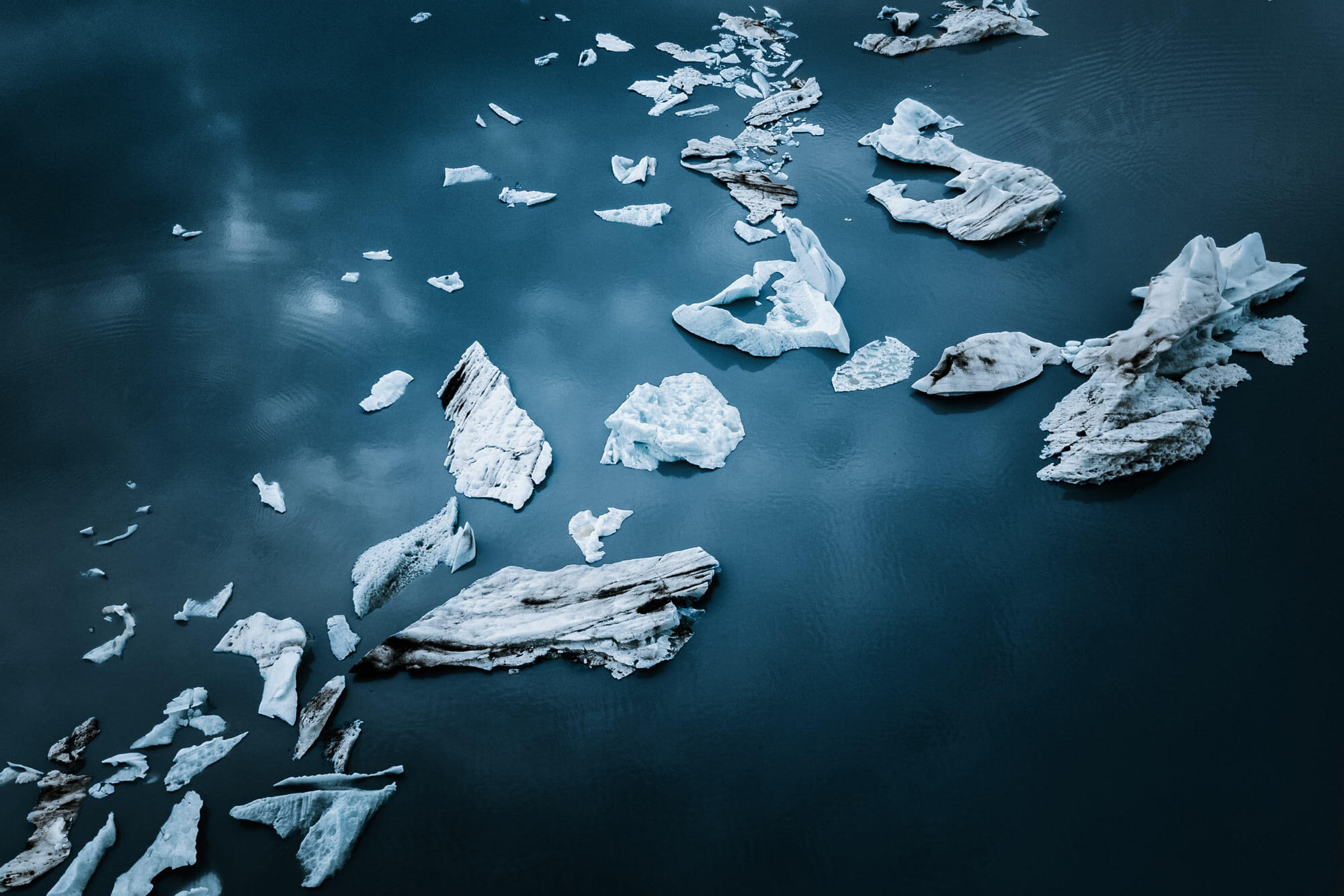 Small white-and-grey icebergs floating on the dark grey ocean partially reflecting a cloudy sky