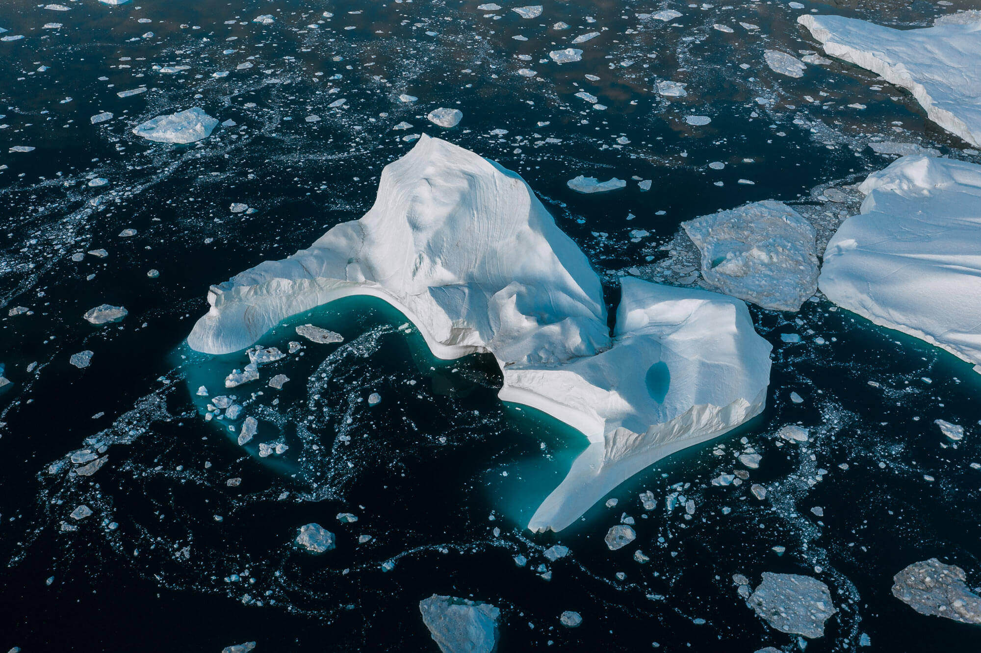 A close-up shot on an iceberg floating in dark blue-green water surrounded by smaller icebergs