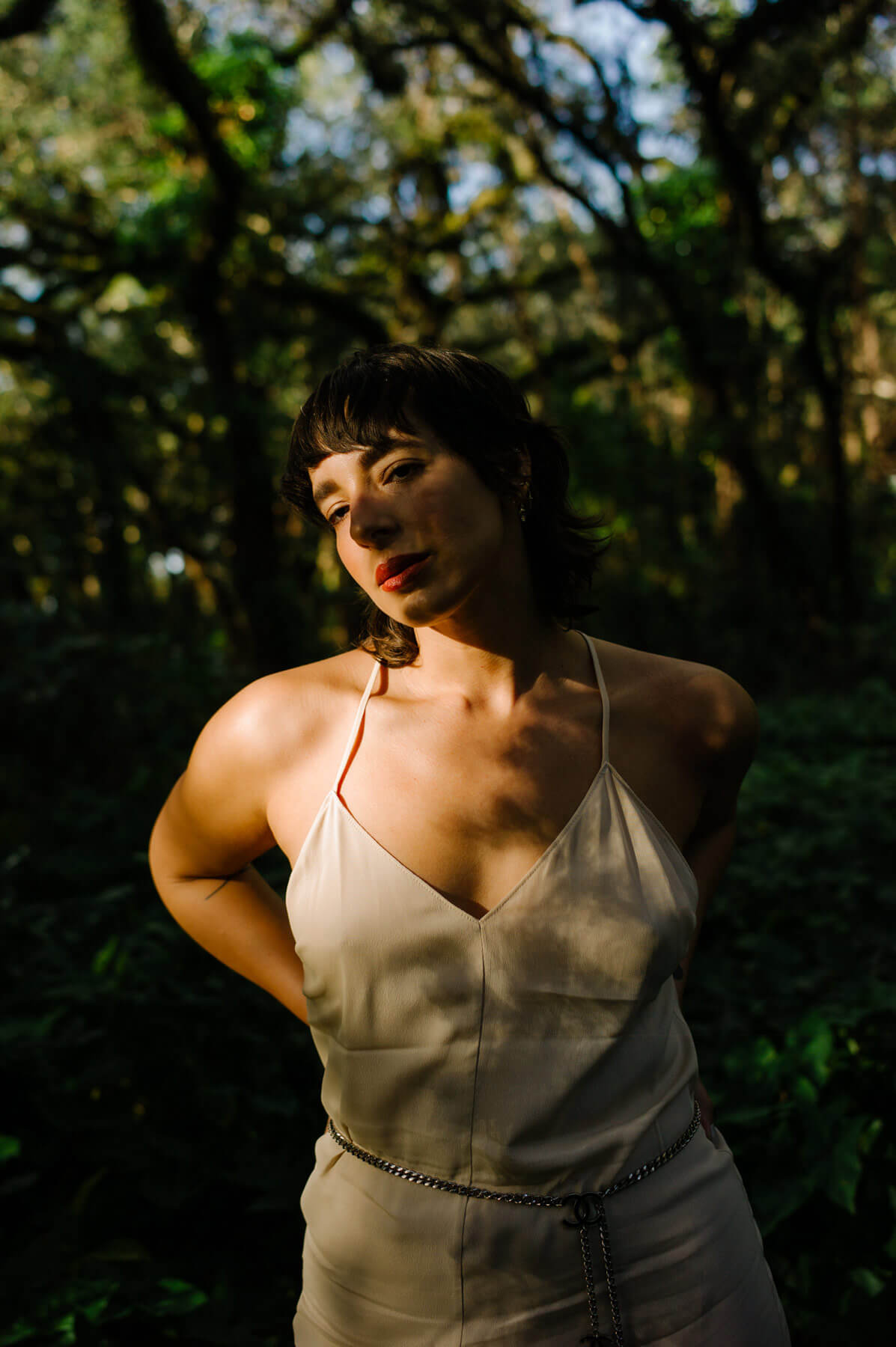 A lady posing for a photo in the shadows of the woods over her face