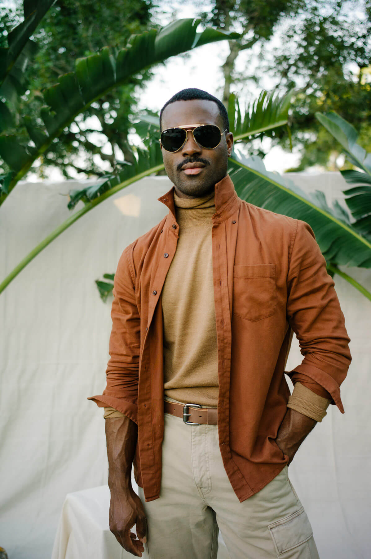 Man wearing sunglasses and brown jacket in garden