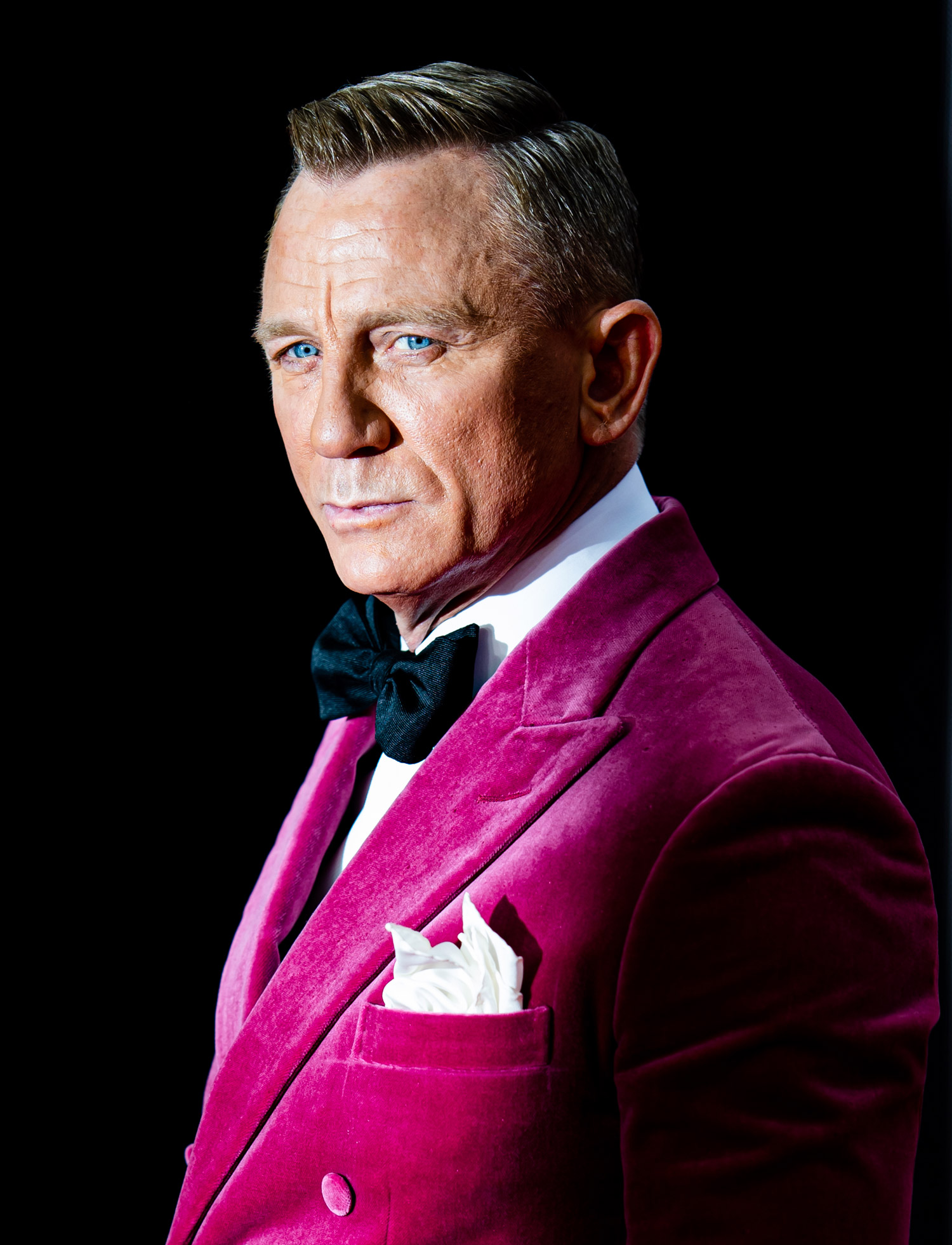 Daniel Craig at the No Time To Die premiere, he is wearing a purple jacket, white shirt and black bow tie.