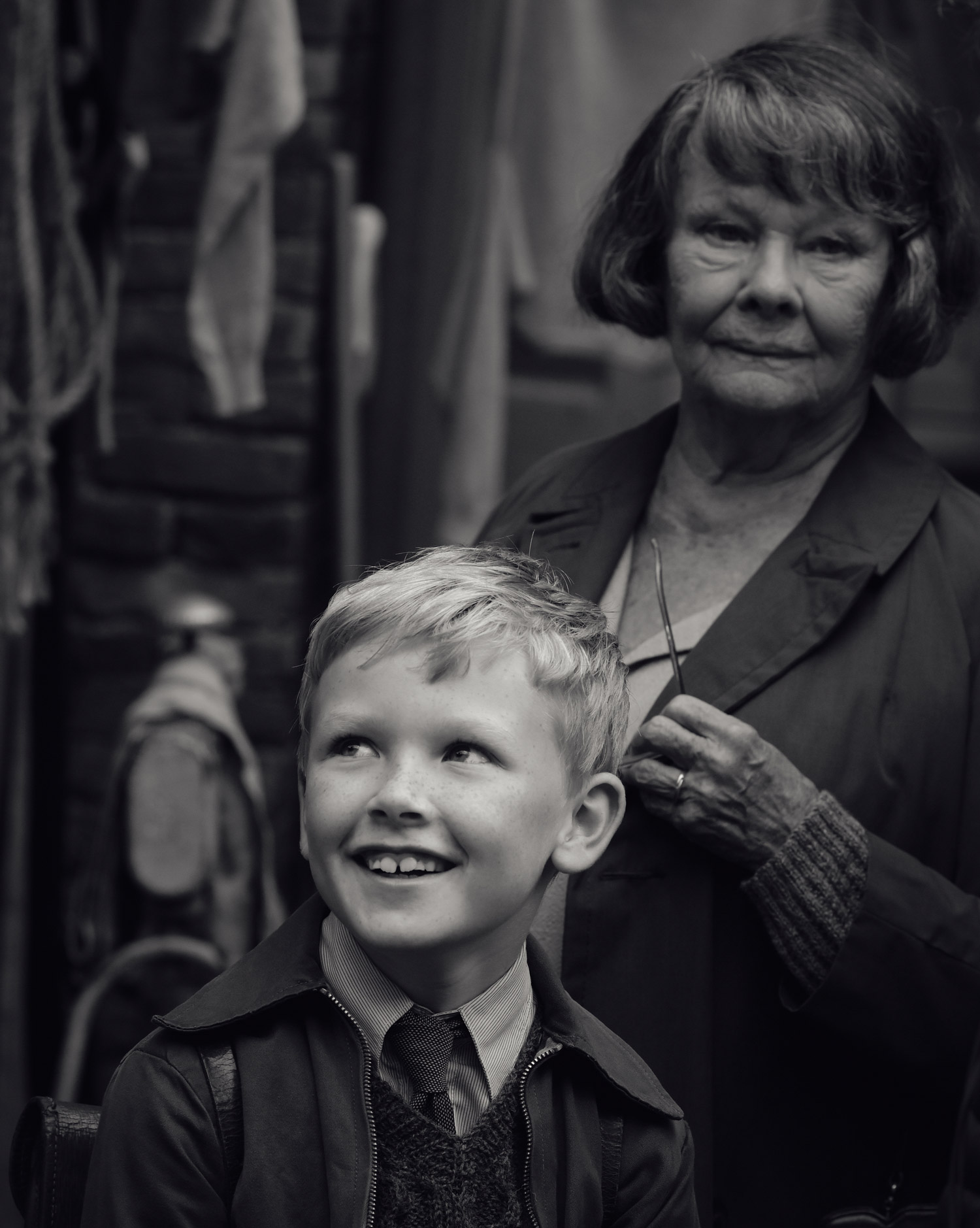 A boy smiles on the set of Belfast, with Judi Dench in the background.