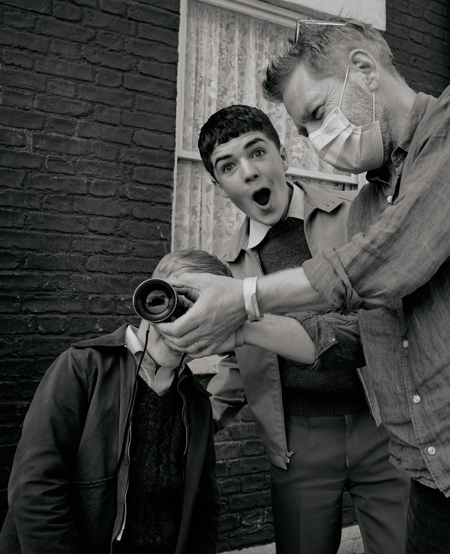 Kenneth Branagh hold a lens for a boy to look into. Another boy has his mouth open.