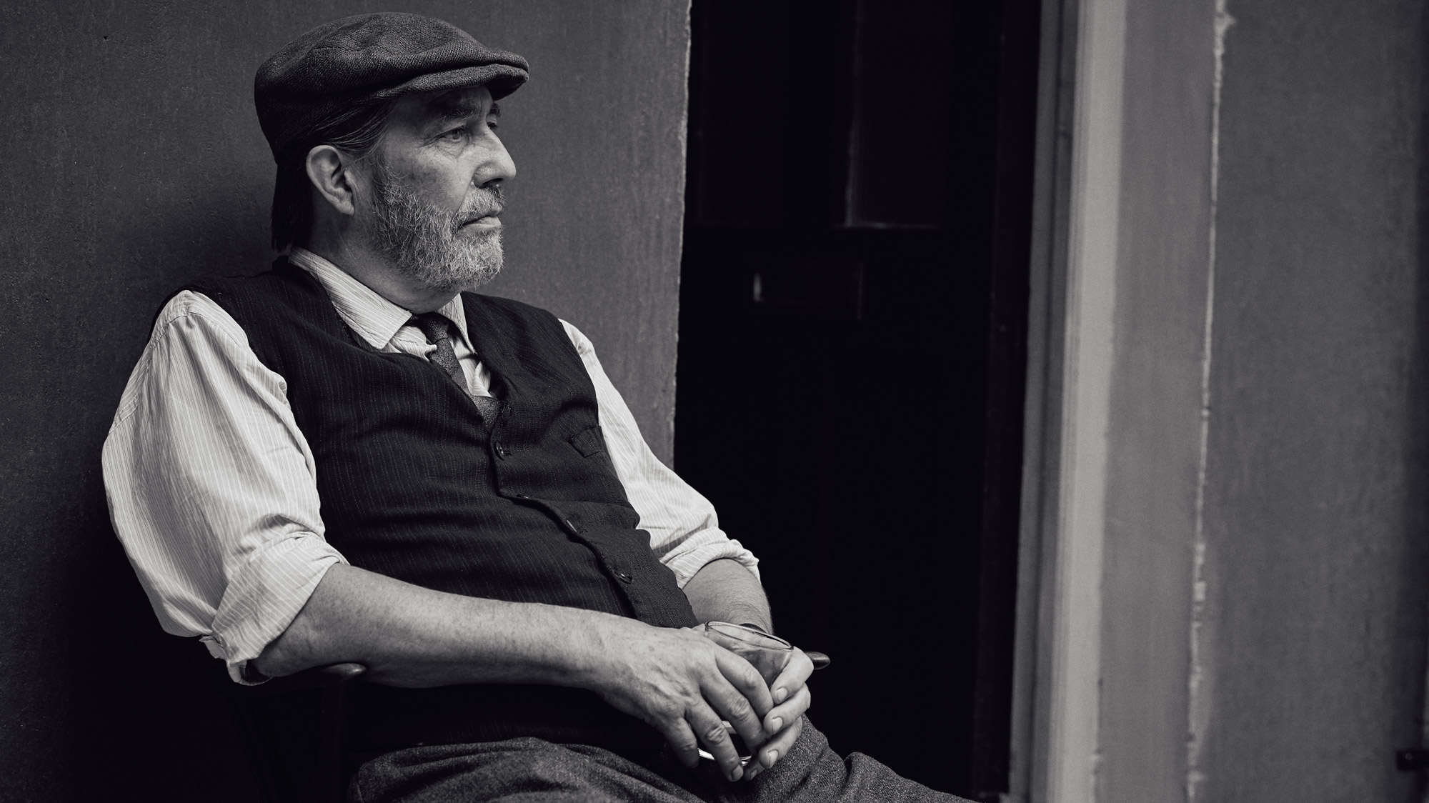 Ciarán Hinds site down holding a drink.