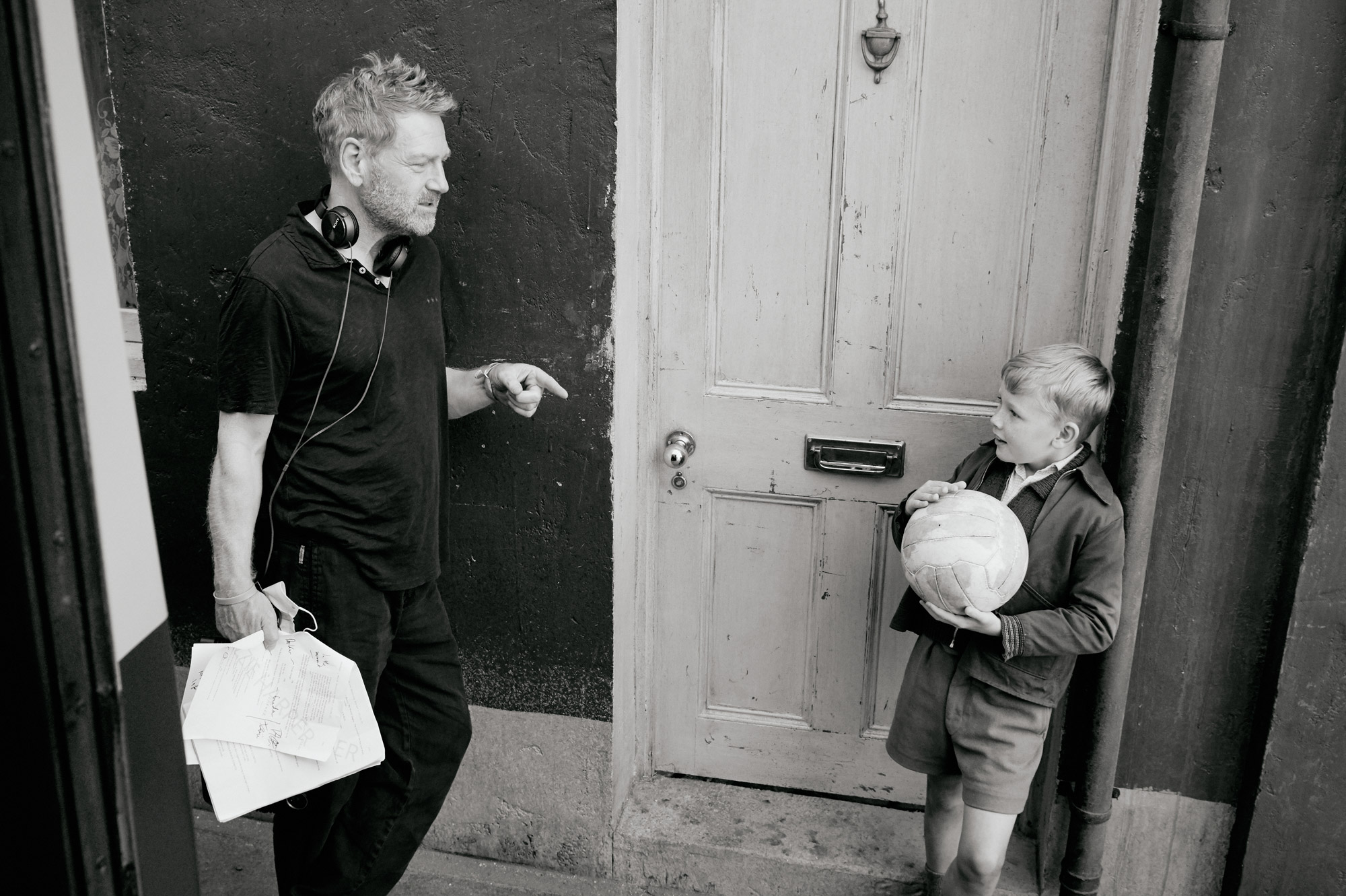 Kenneth Branagh talks to a boy who is holding a ball on the set of Belfast.