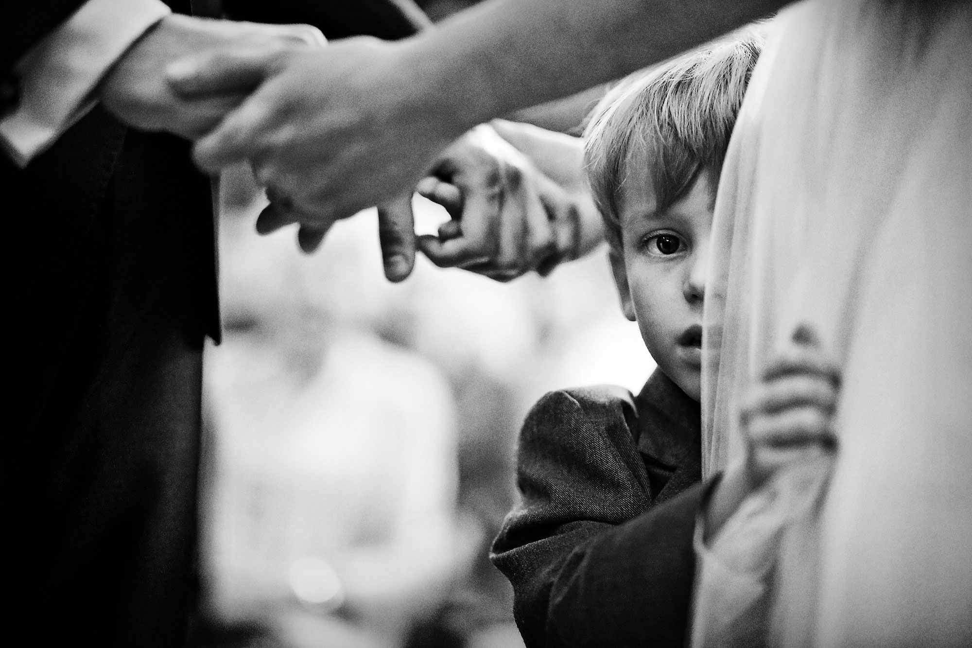 A young boy holding the dress of a bride while staring directly at the camera