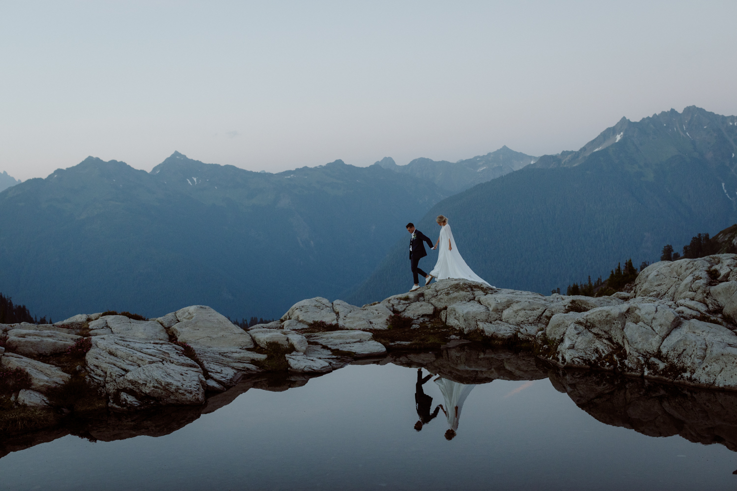 A wedding couple walking over a pond by Cedar and Pines