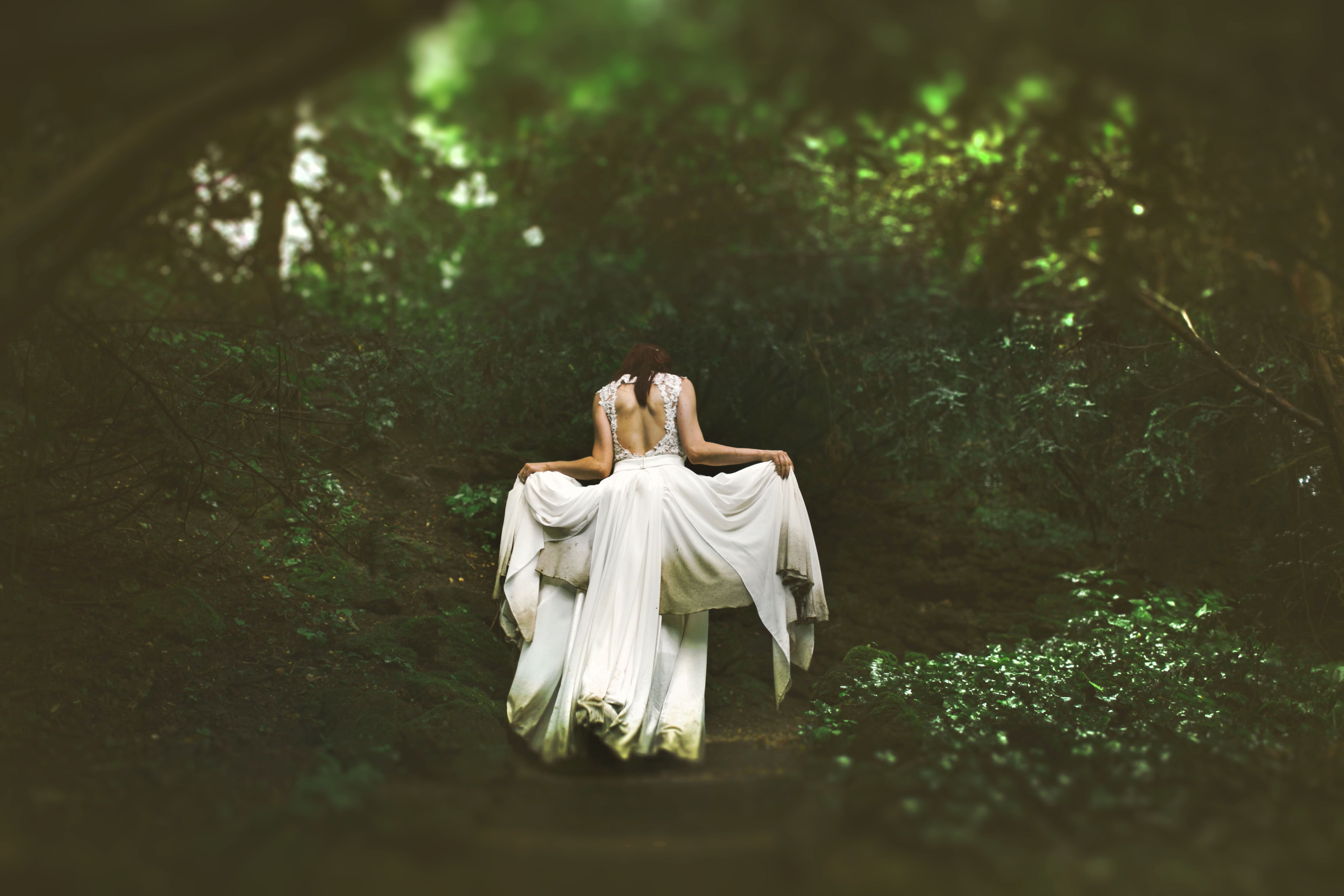 A woman in a wedding dress walks through a forest