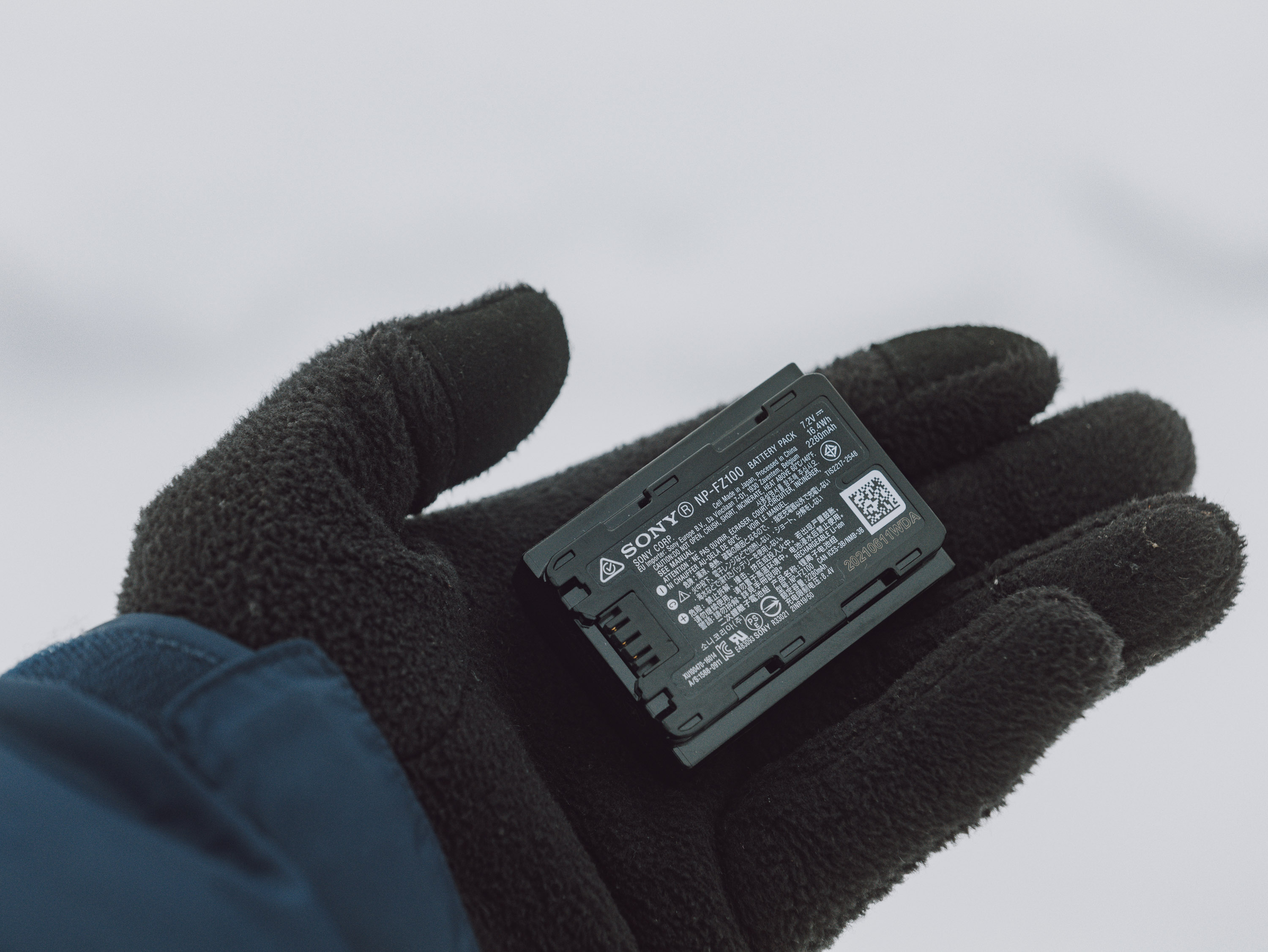 Close up shot of a hand with a glove holding a camera battery.