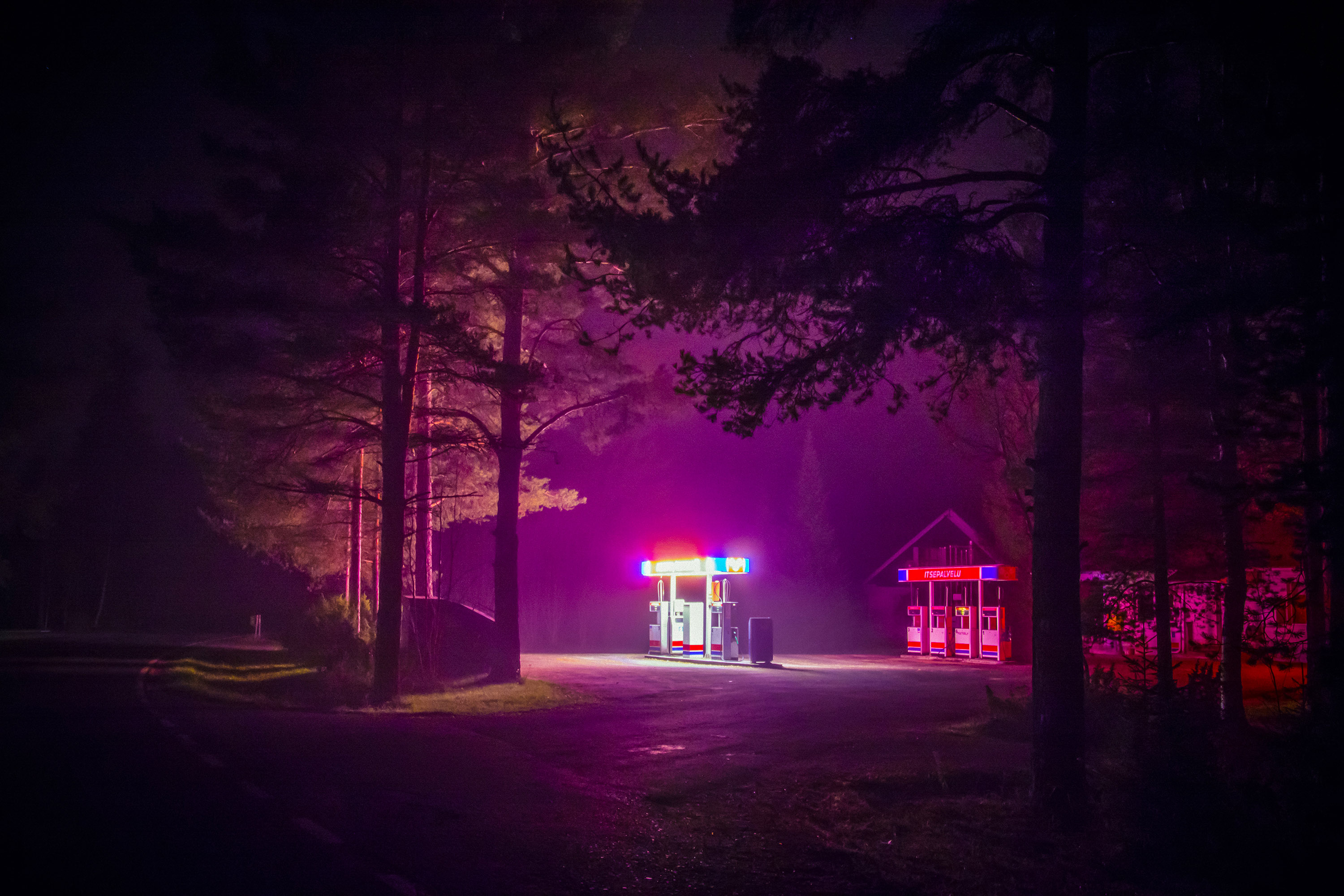 A neon magenta image of a petrol station glowing amidst the trees
