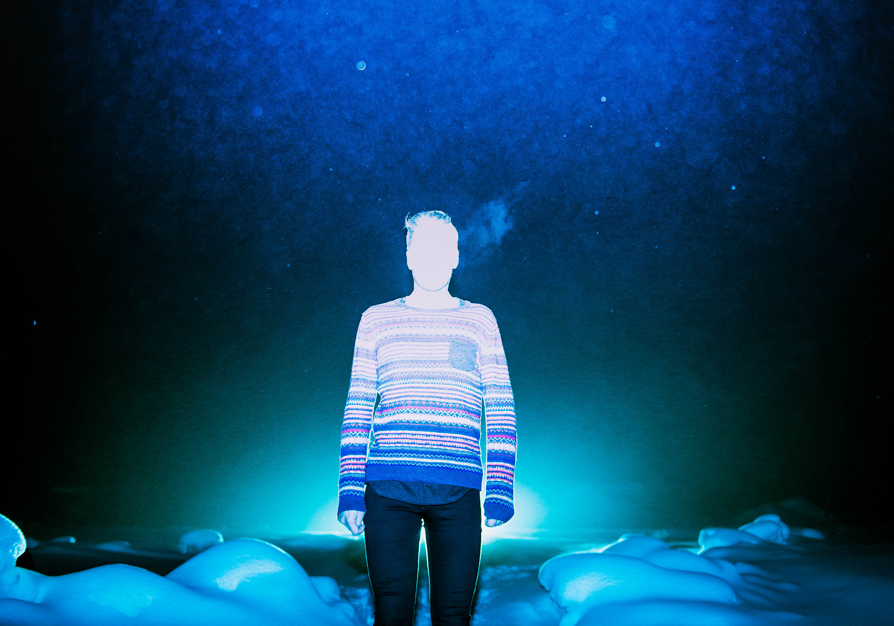 a heavily lit blue cast photo of a man stood in front of a snowy wintery landscape