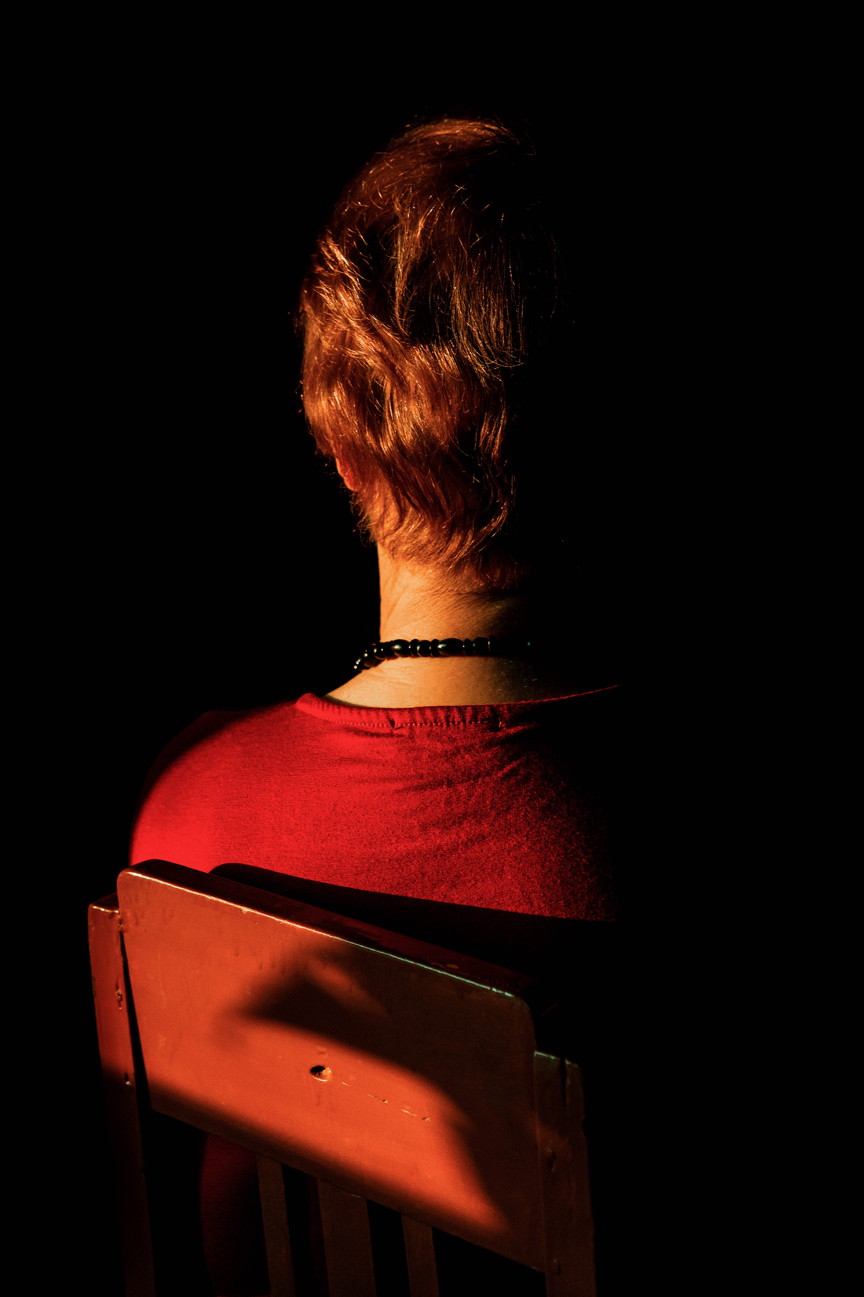 A warm coloured image from behind  of a woman with short hair sat on a chair