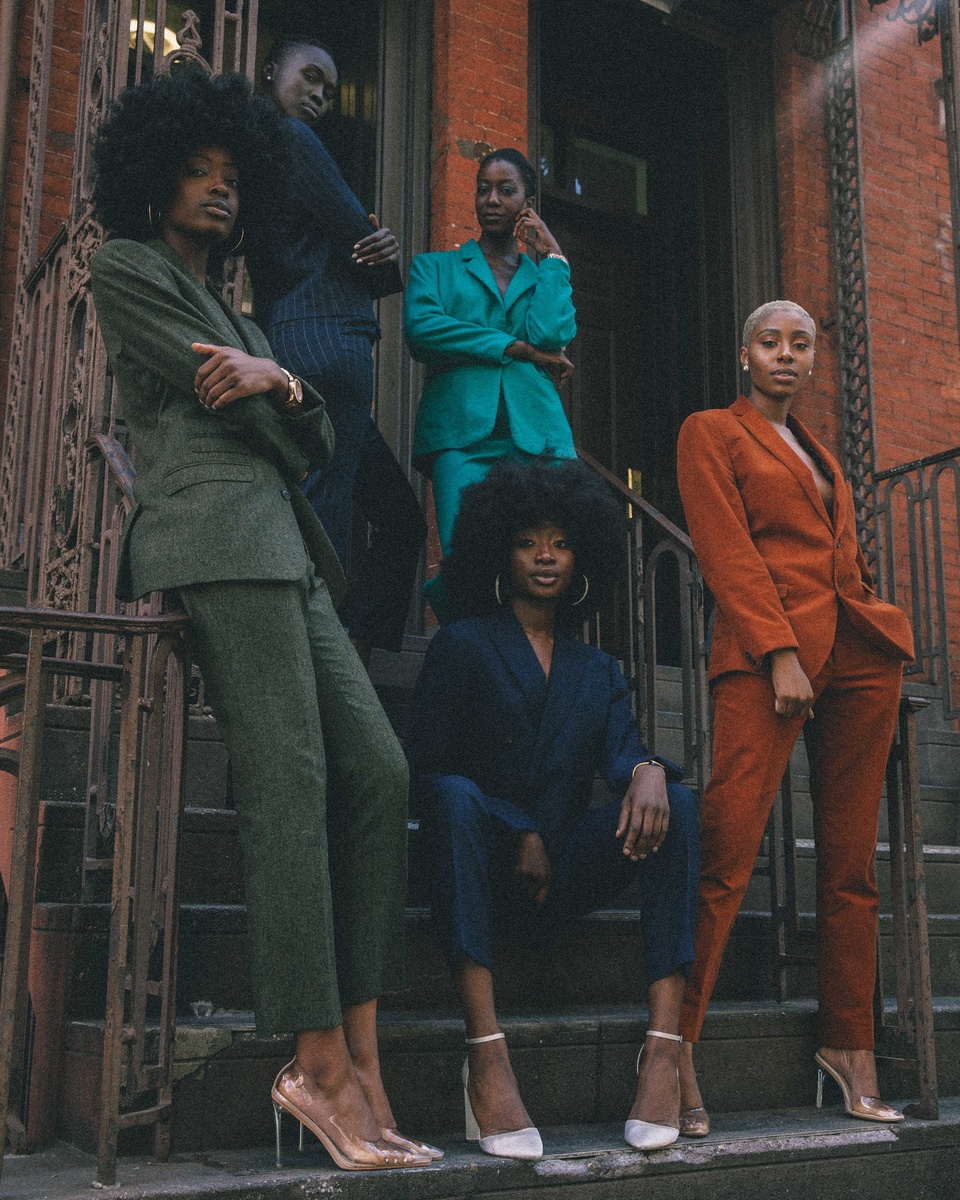 A group of people wearing different-coloured suits—some sitting, some standing and looking at the camera.