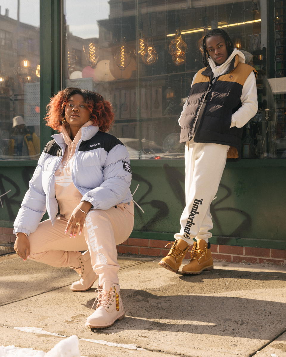 A black woman crouching down on a sidewalk while a black man leans against a shop window behind her