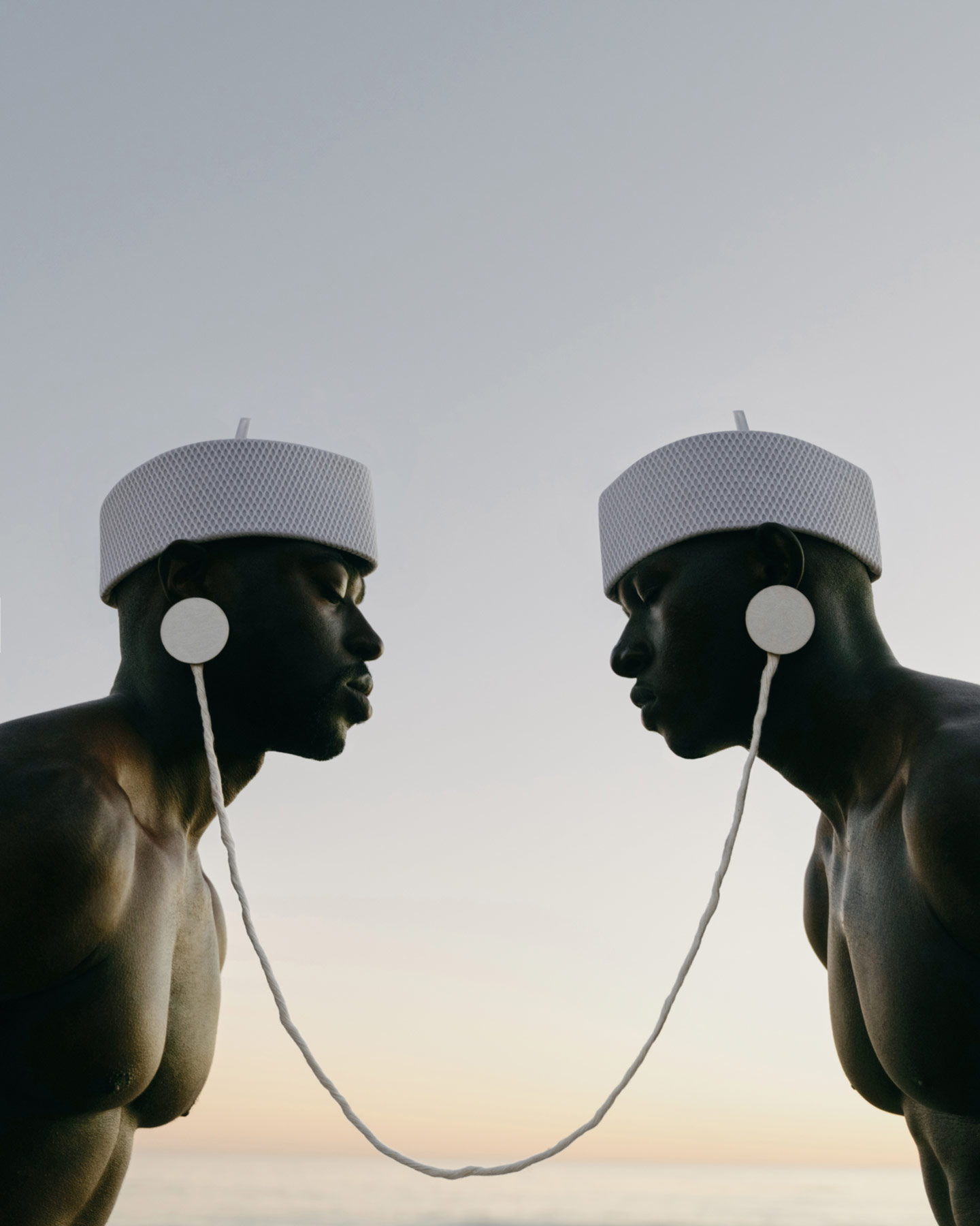 Two black men wearing white hats with their ears connected by white headphones