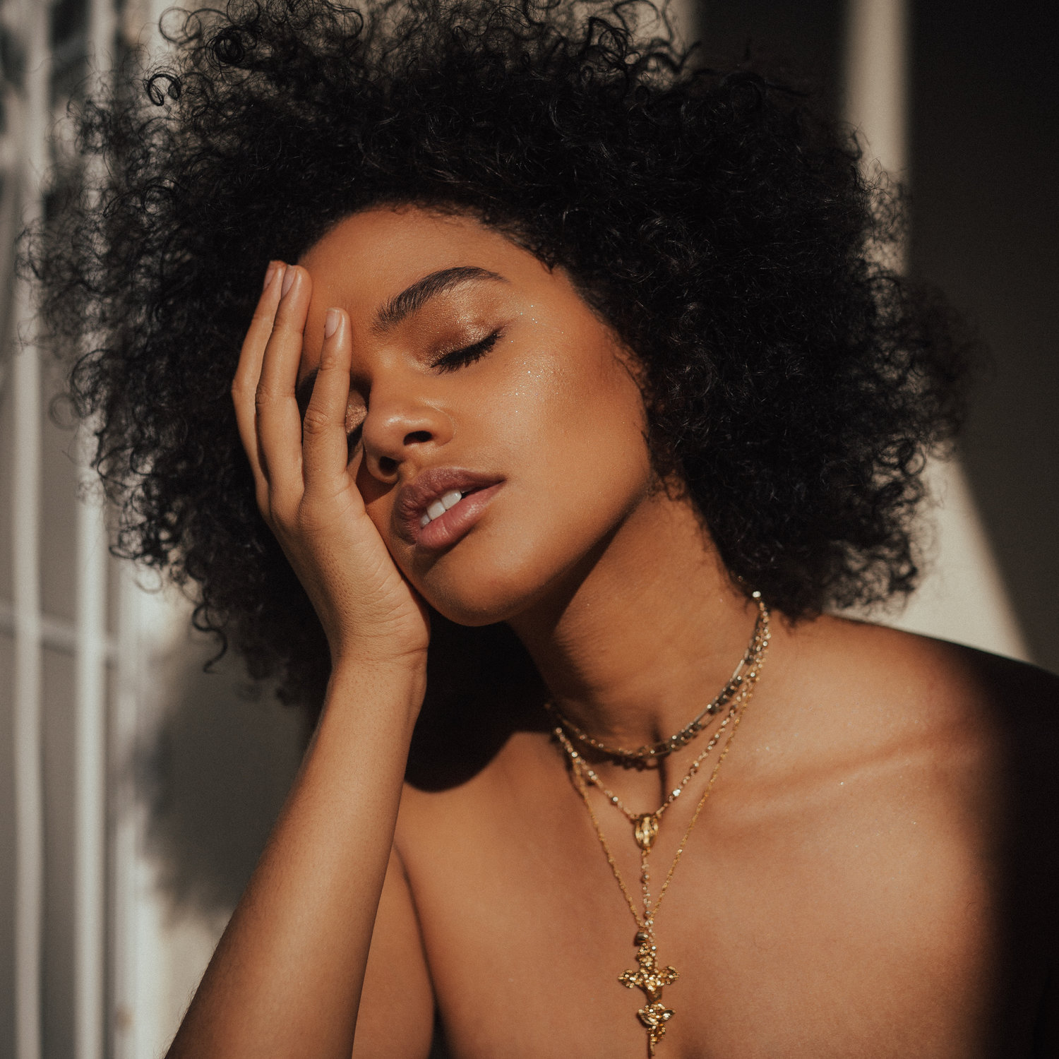 A black woman wearing a gold necklace with her eyes shut holding her hand to her face
