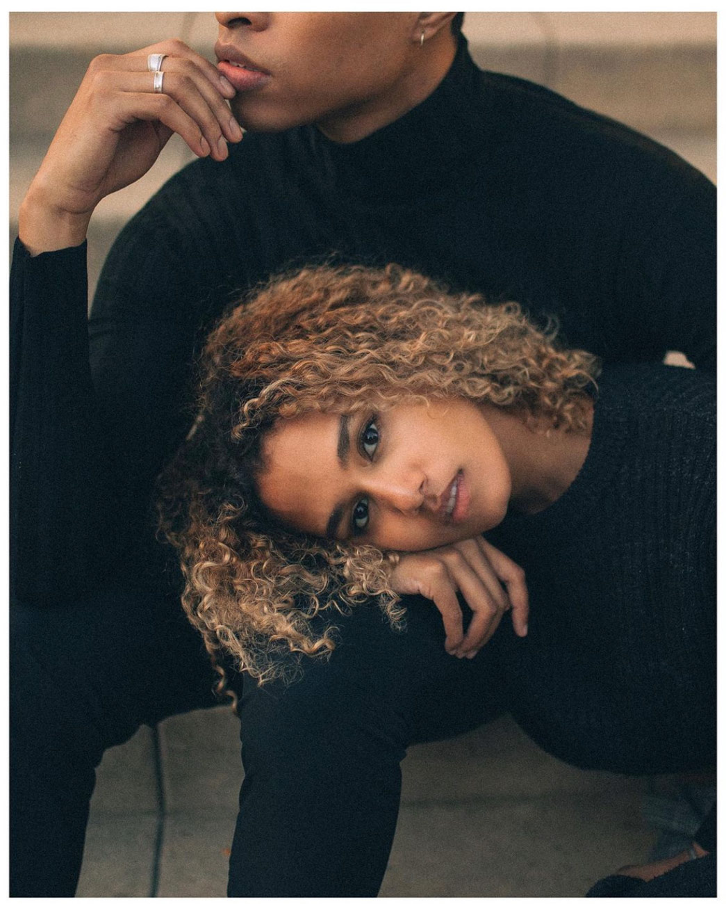 A Black man and woman, the woman lying on the man's lap looking at the camera while the man is out of frame looking away
