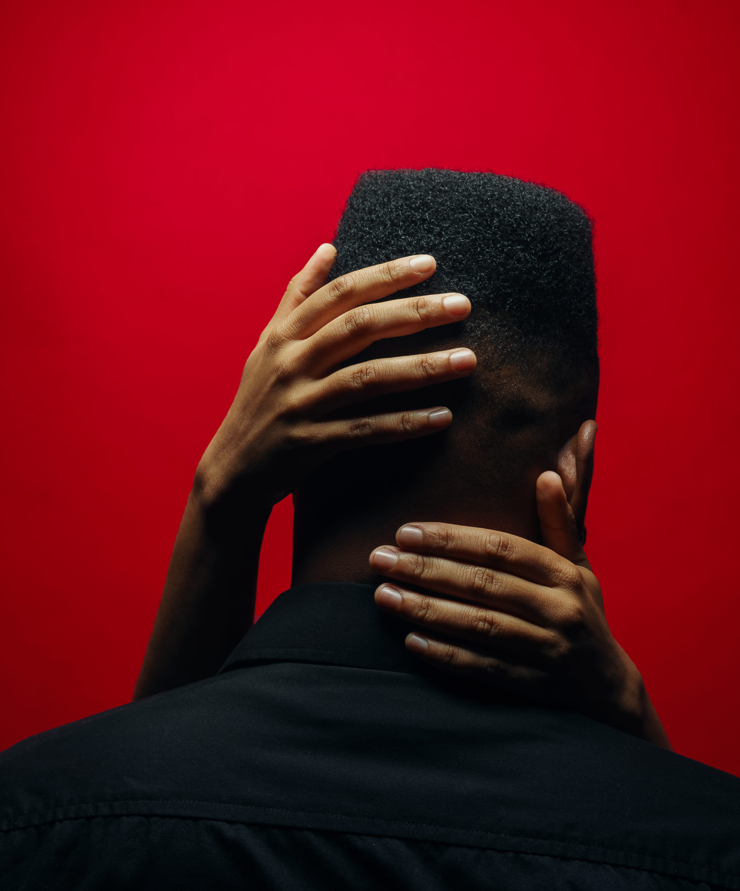 A black person with their back to the camera against a red background a pair of hands holding their head