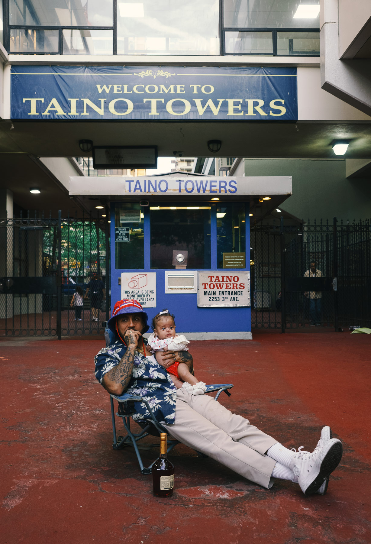 A parent and their child sitting in front of a building with a sign saying welcome to taino towers