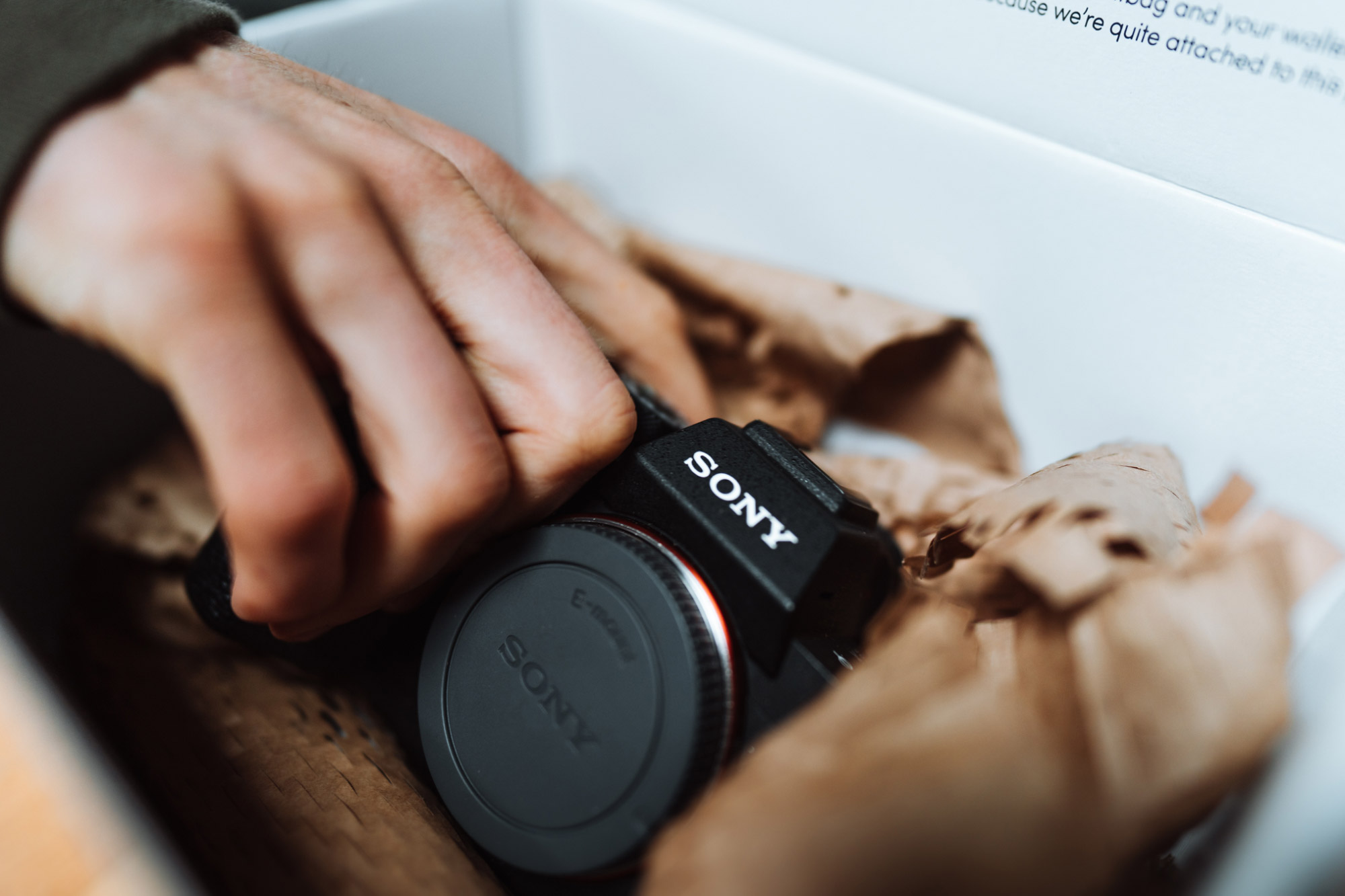 A hand reaches into a box containing a Sony A7R III camera, with brown paper surrounding the camera.