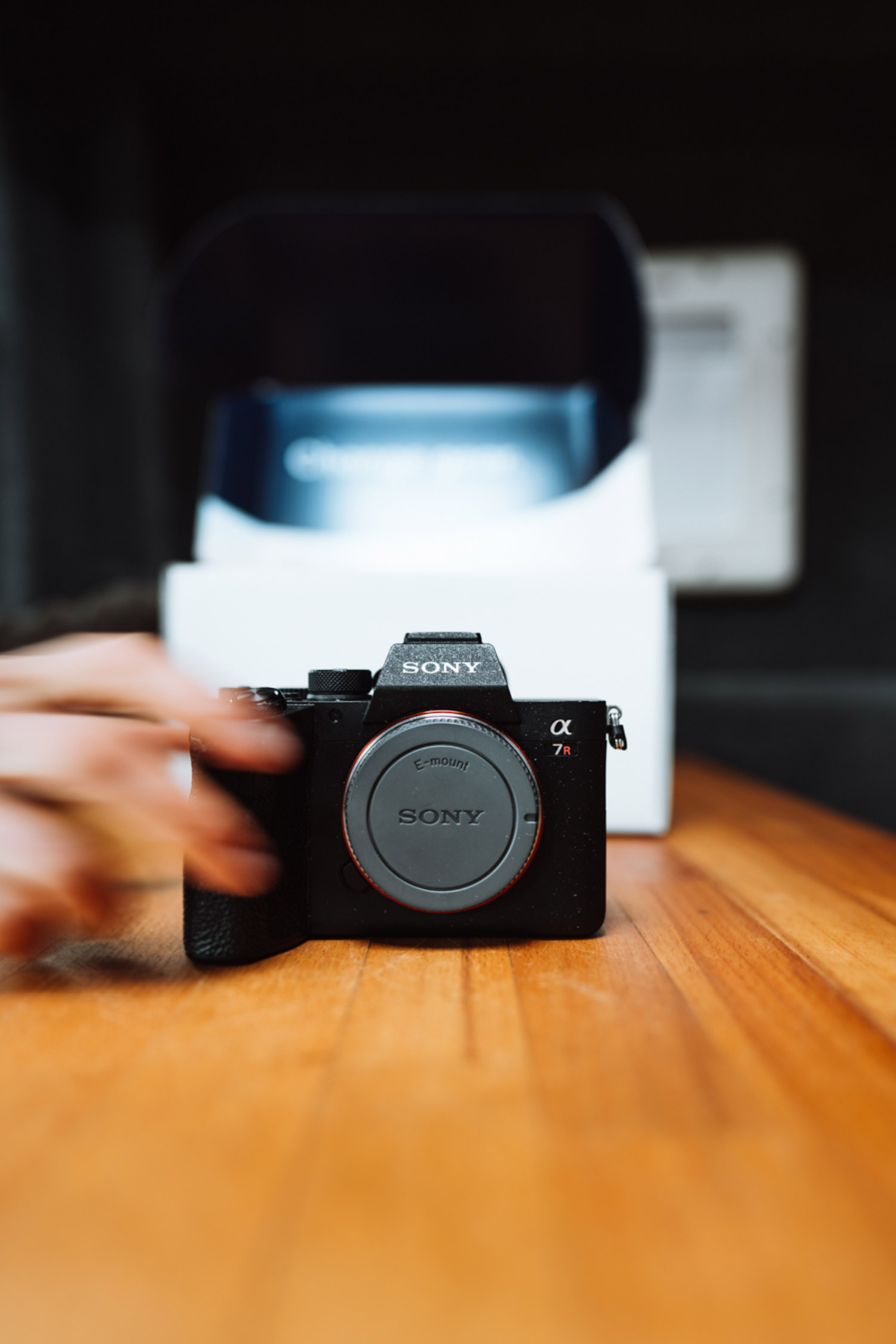 A Sony AR7 sits on a wooden table in front of MPB packaging. A blurred hand reaches for the camera.