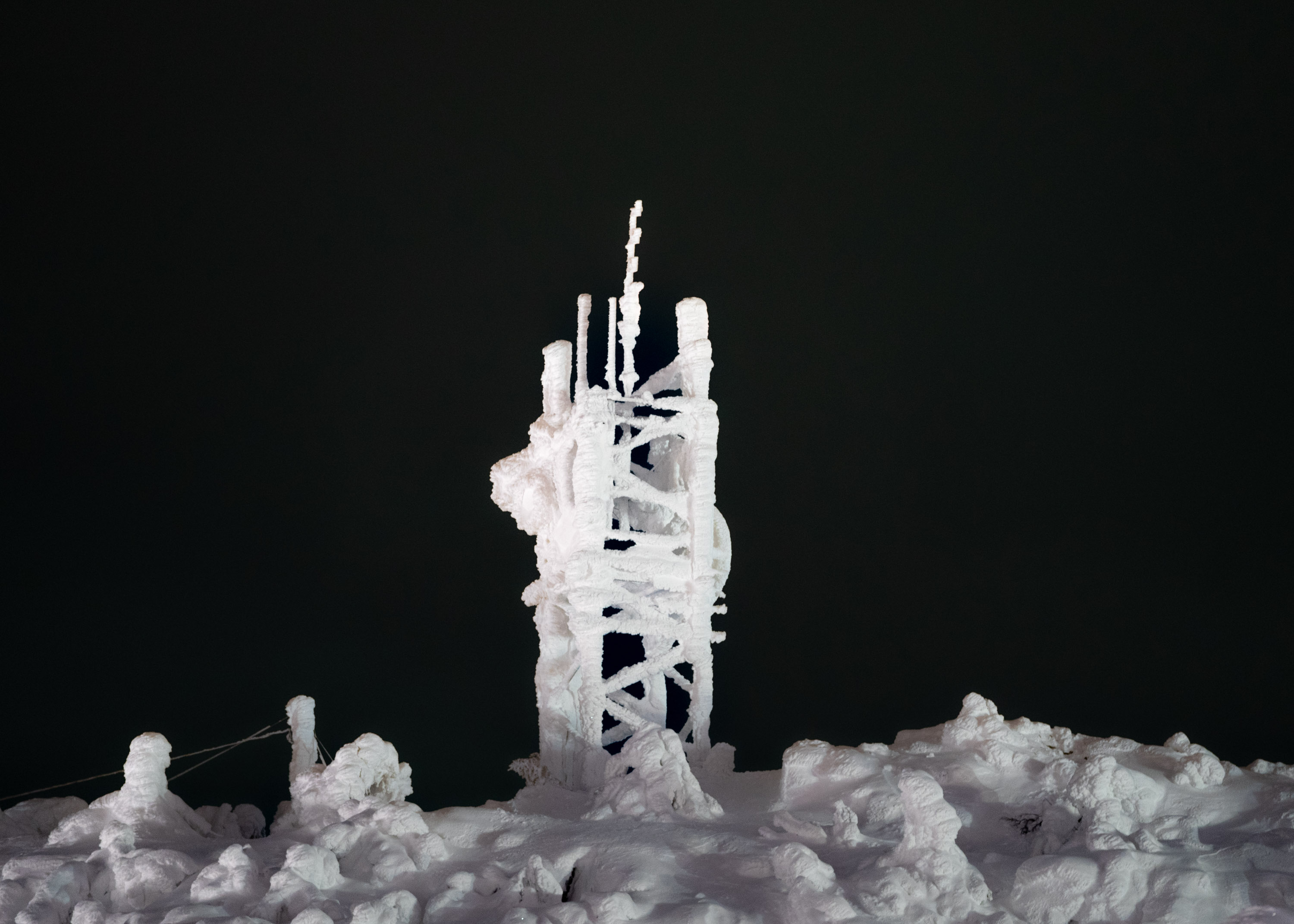 A telephone mast covered in snow shot at night with a black background.