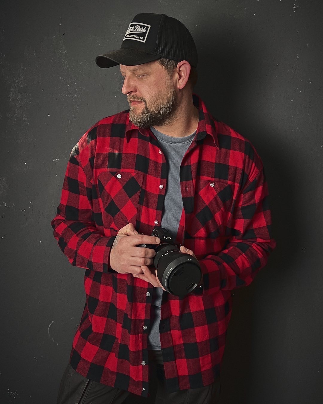  Fotograf Thomas Popien in einem Flanellhemd vor einem schwarzen Hintergrund mit einer Kamera in der Hand 