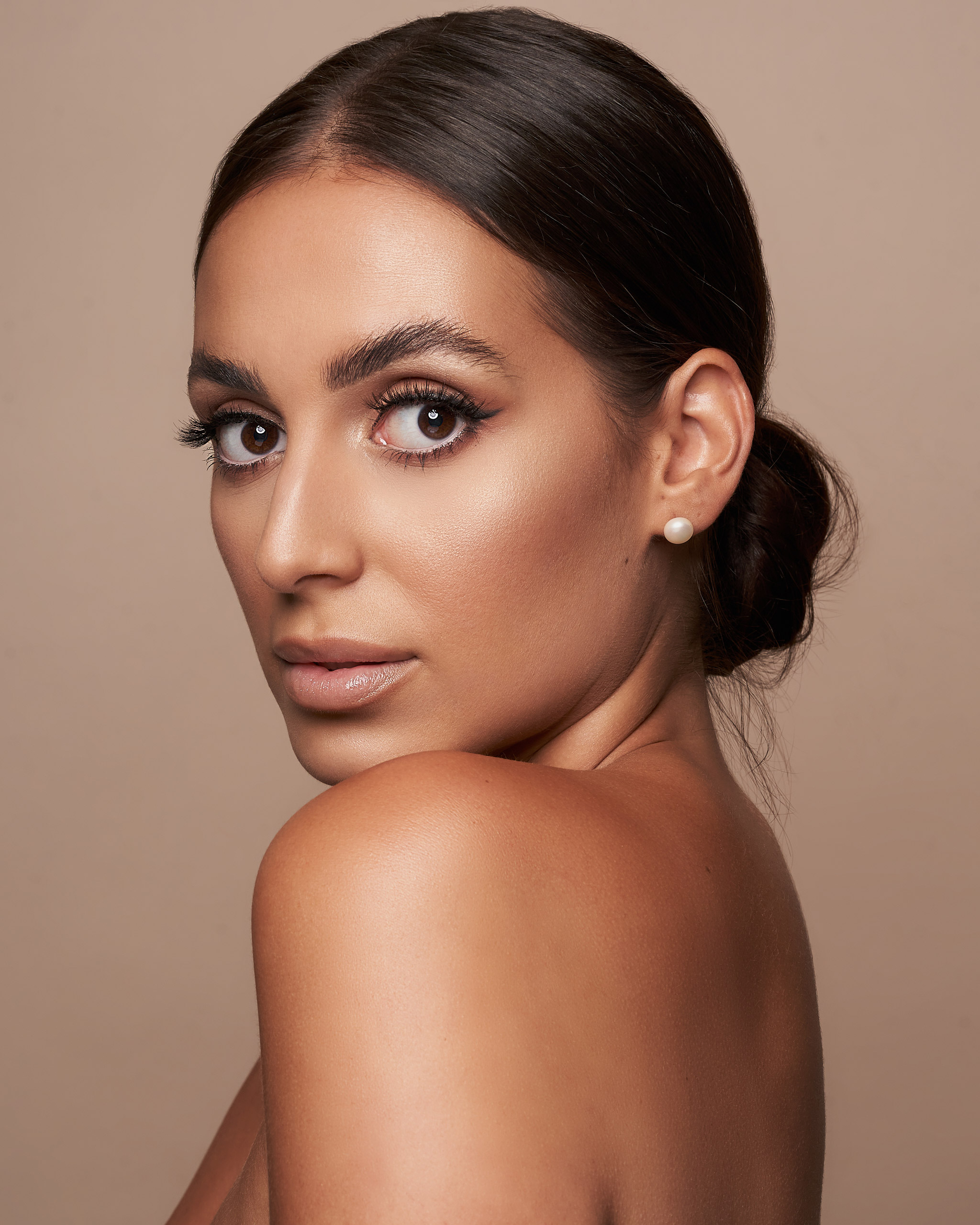 Porträtaufnahme eines Models, Natalia Garcia, mit einem eleganten Dutt, das ihr über die Schulter schaut, mit Make-up von Natalia Garcia 