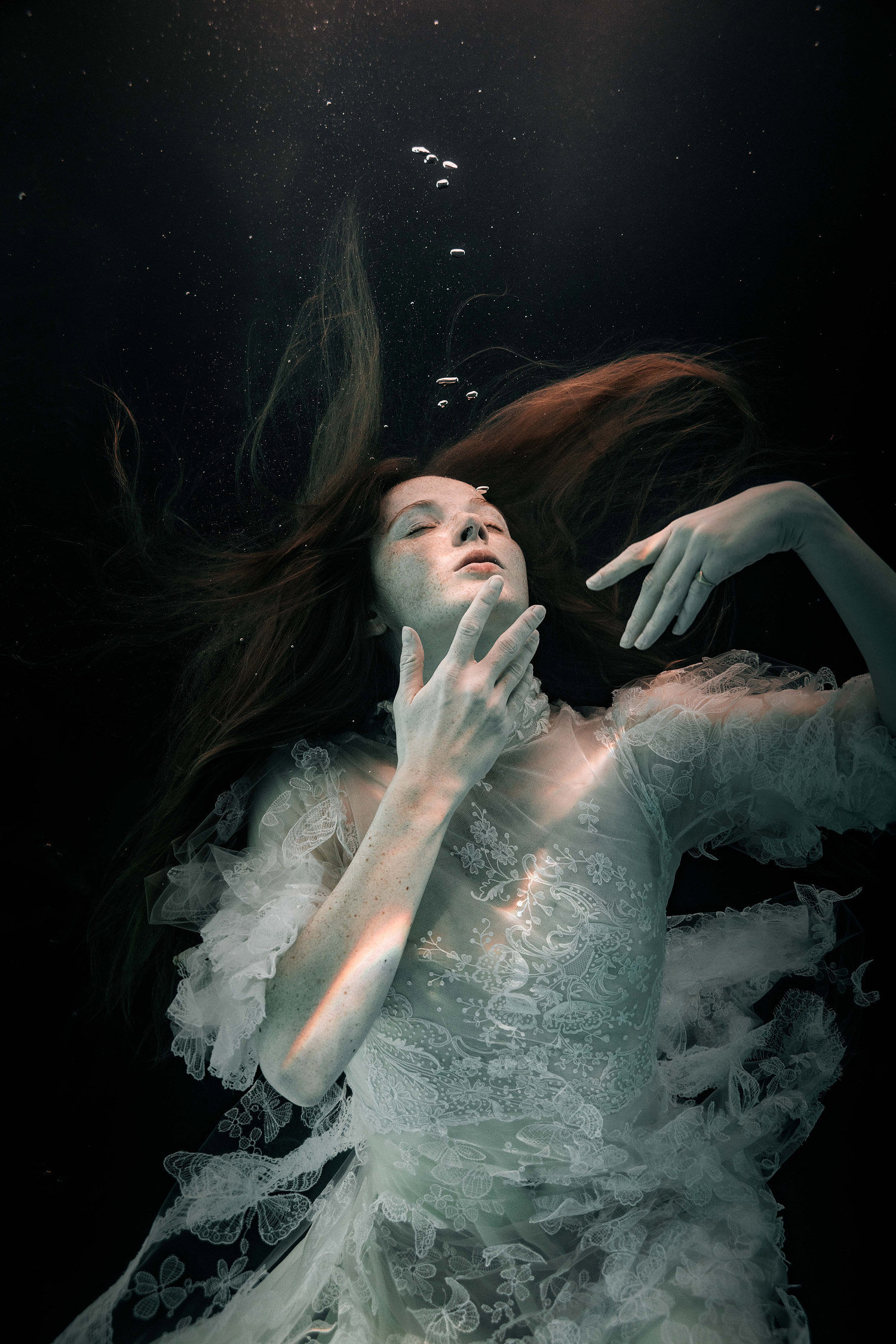 A woman under water with red hair and a white dress.