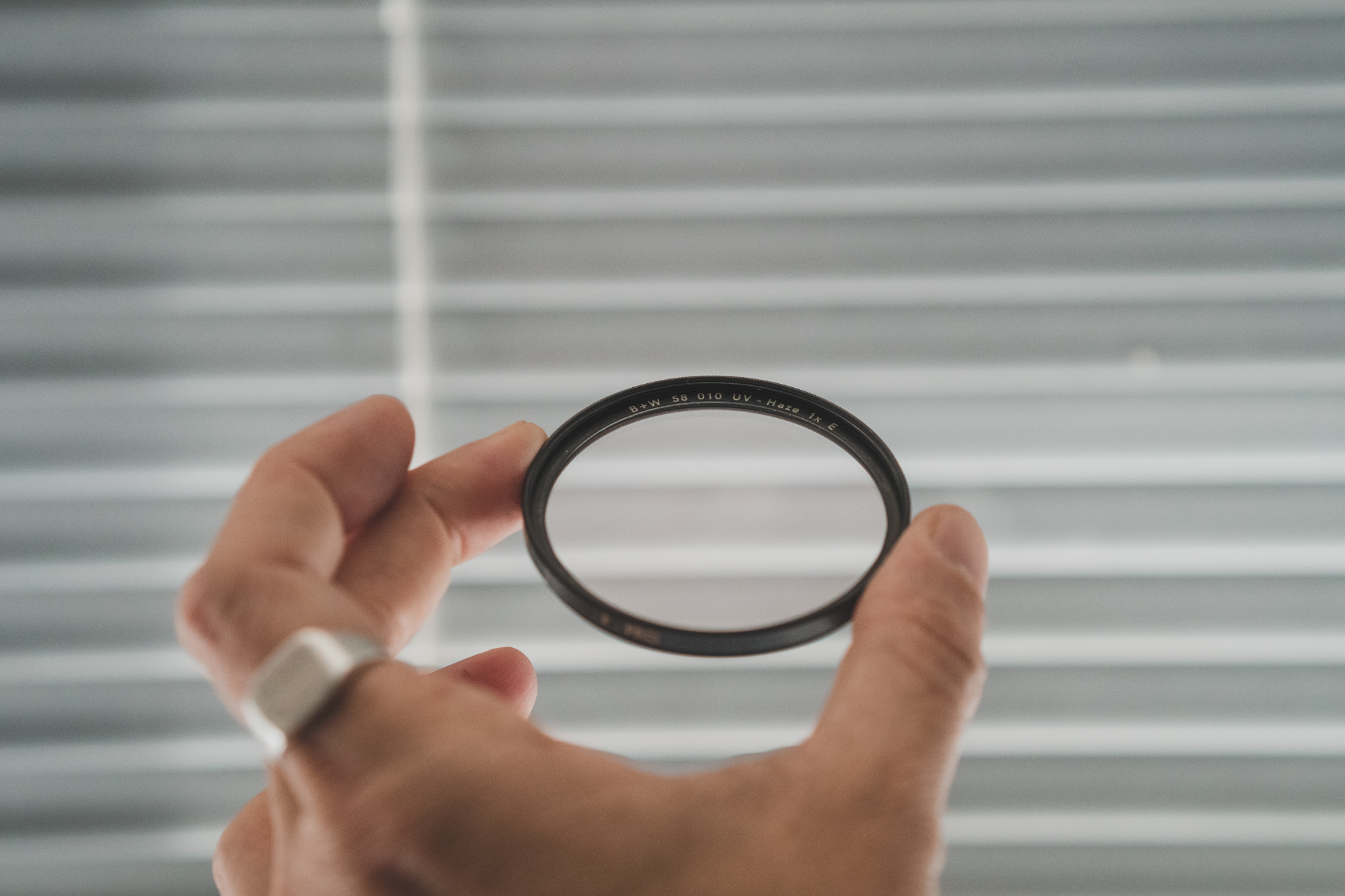 Een hand met een zilveren ring die een zwart-wit UV-filter vasthoudt.