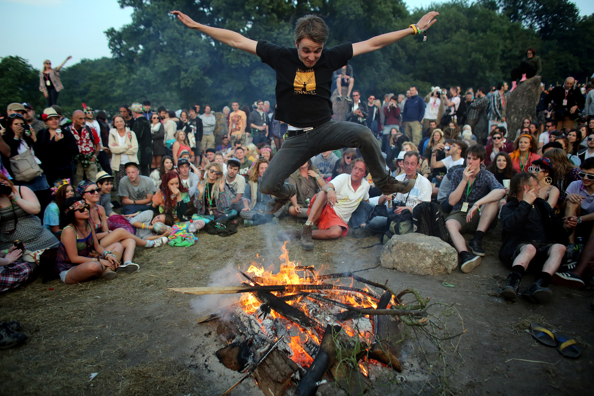 A person jumps over a fire that has been lit inside the stone circle as people gather for sunset at the Glastonbury Festival of Contemporary Performing Arts site at Worthy Farm, Pilton on June 26, 2013.