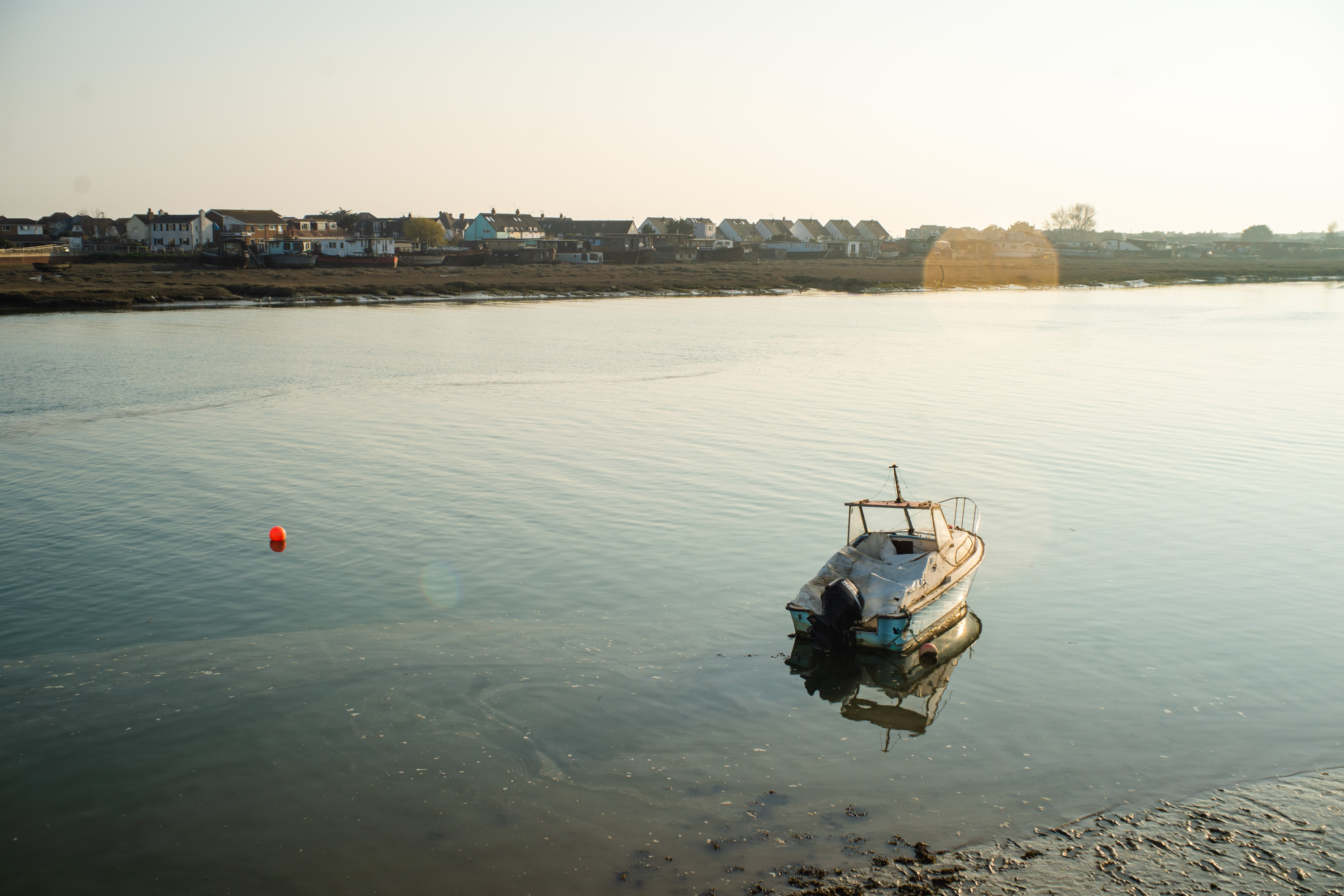 A picture of a boat in a river in the evening with lens flare