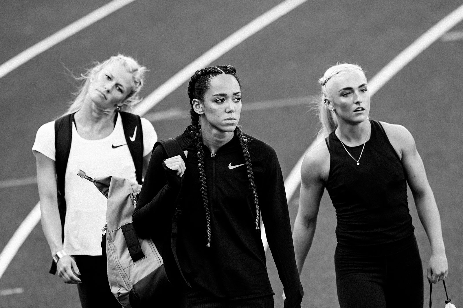 Zwart-witfoto van drie atleten in Nike-uitrusting op een atletiekbaan.