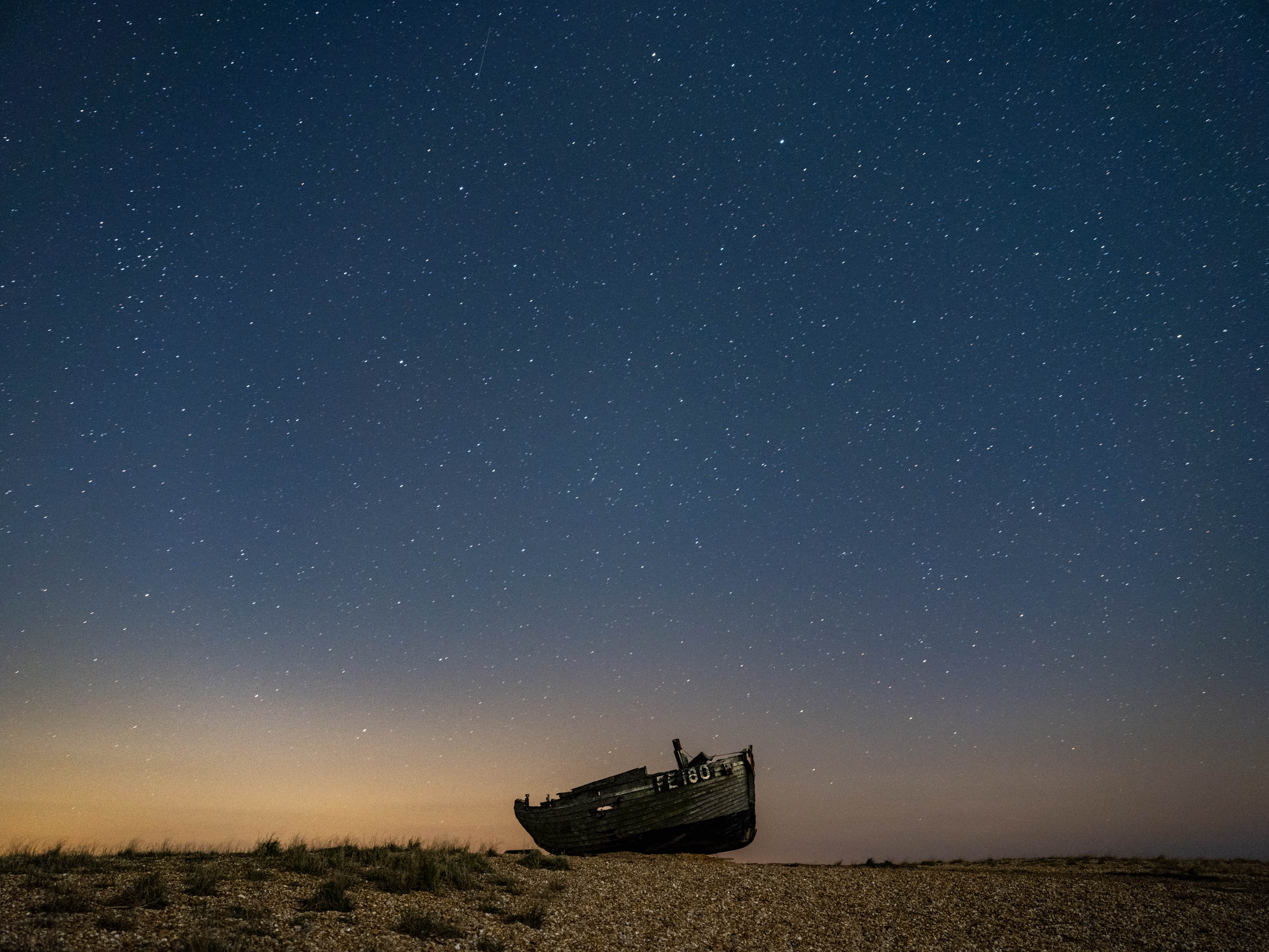 Een vissersboot ligt op een kiezelstrand voor de nachtelijke hemel